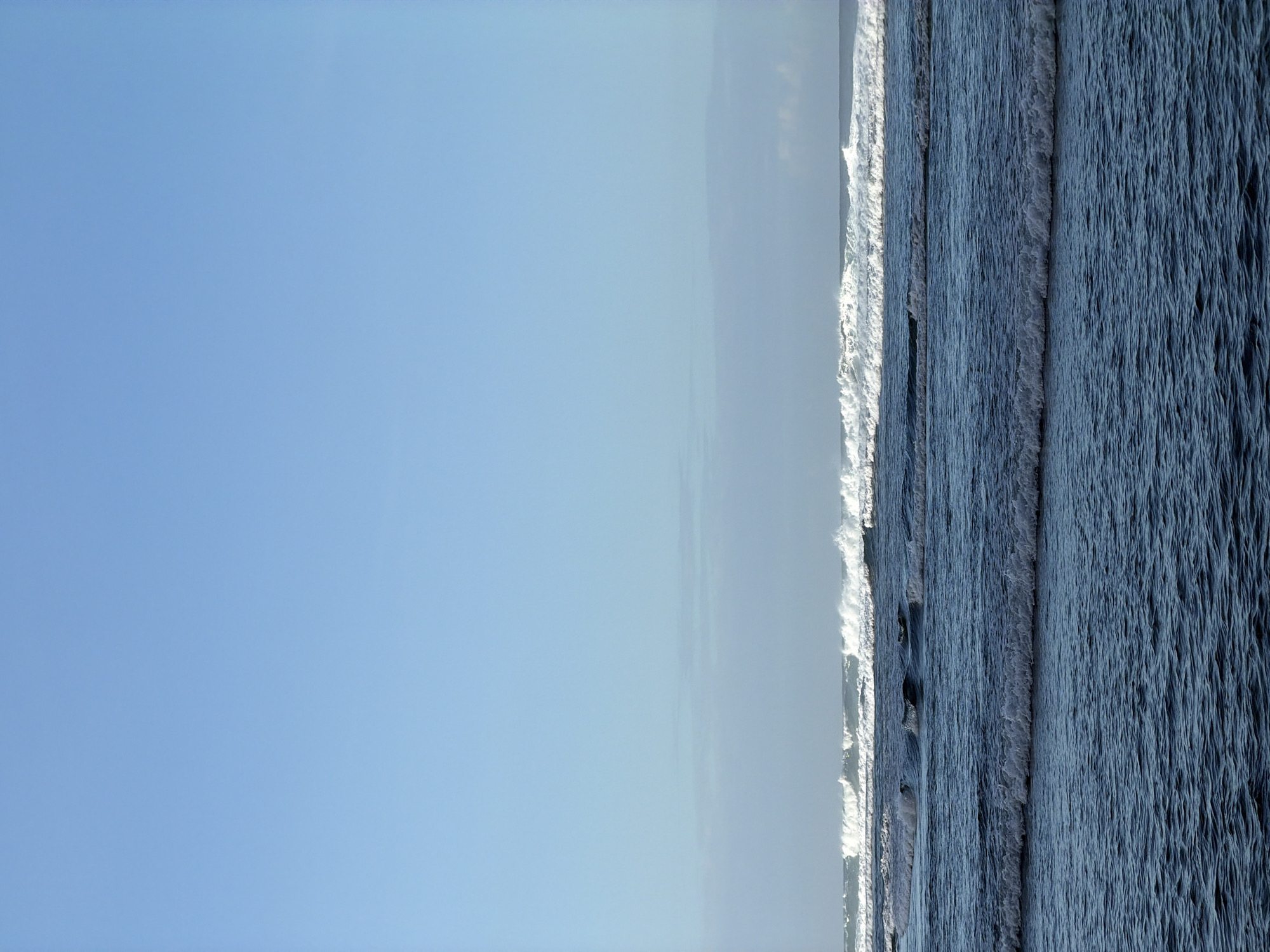 The image presents an ocean view, notably featuring prominent waves. The sky occupies the left portion of the frame, transitioning into a horizon line towards the middle. The right side of the image is filled with the sea, showcasing the texture and motion of the waves. The image appears to be taken at Kuta Selatan, Indonesia.