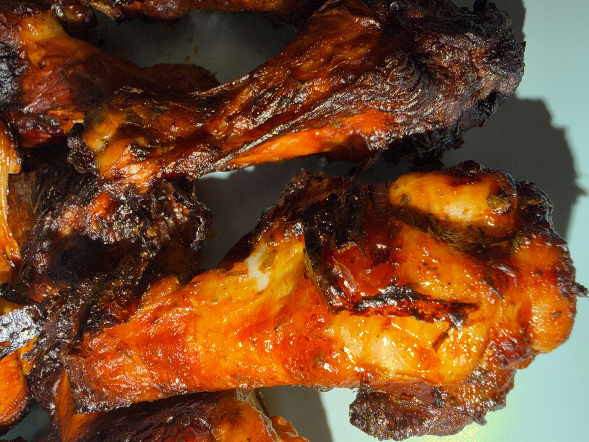 The image is a close-up, overhead shot of several roasted chicken drumsticks, some appearing slightly charred. They are arranged on a light blue surface, casting shadows. There are no people or any contextual elements that would indicate a specific location in Bila Tserkva, Ukraine, or anywhere else. The focus is solely on the food.