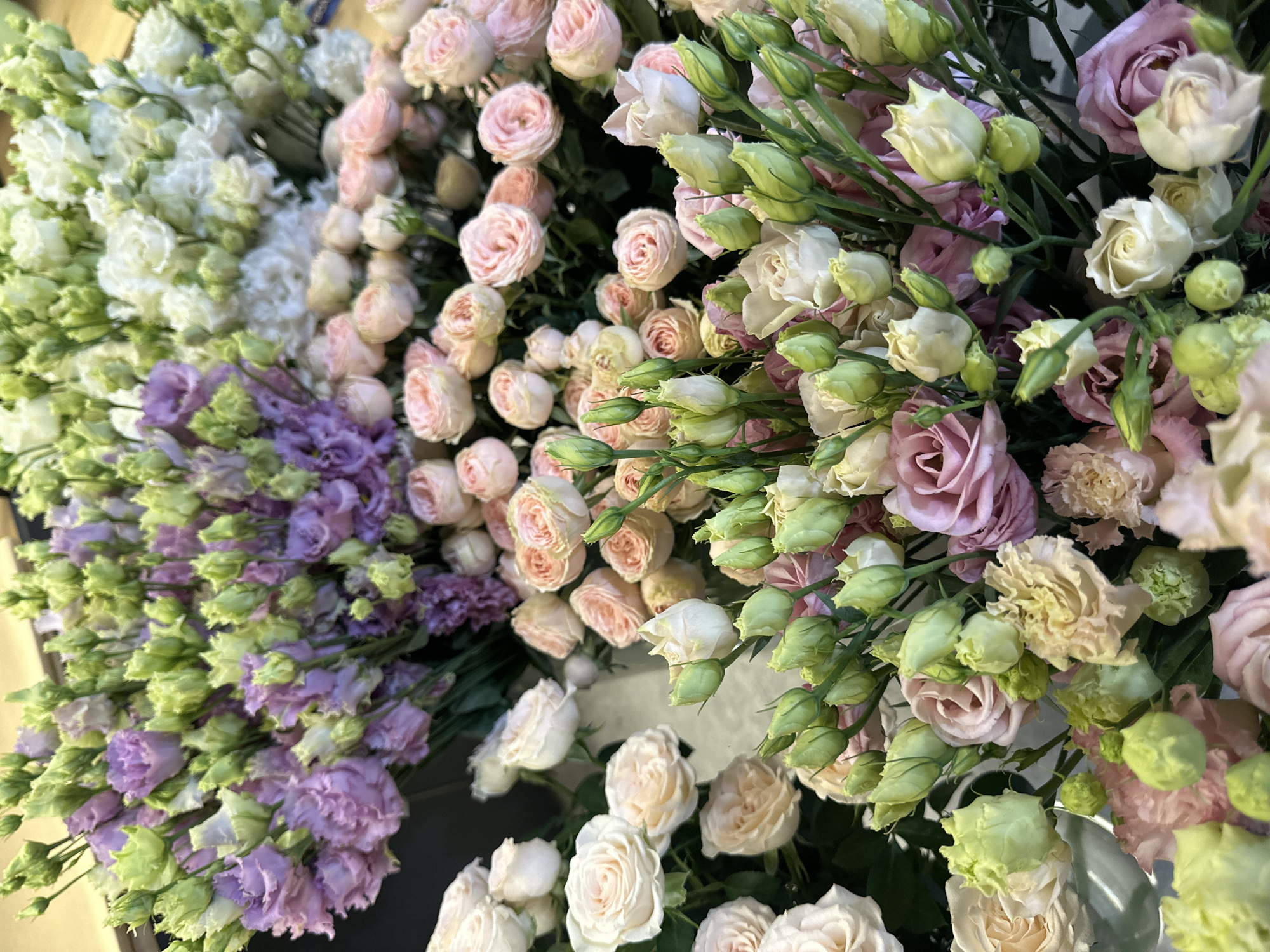 The image shows a close-up, high-angle view of several bunches of flowers. The flowers are a variety of colors including white, pink, and purple. There are roses and other types of flowers with many buds. The focus is sharp, allowing for clear observation of the flower petals and stems. The background is blurred and out of focus. There is no discernible information to indicate the location as Chișinău, Moldova. There are no people visible in the image.