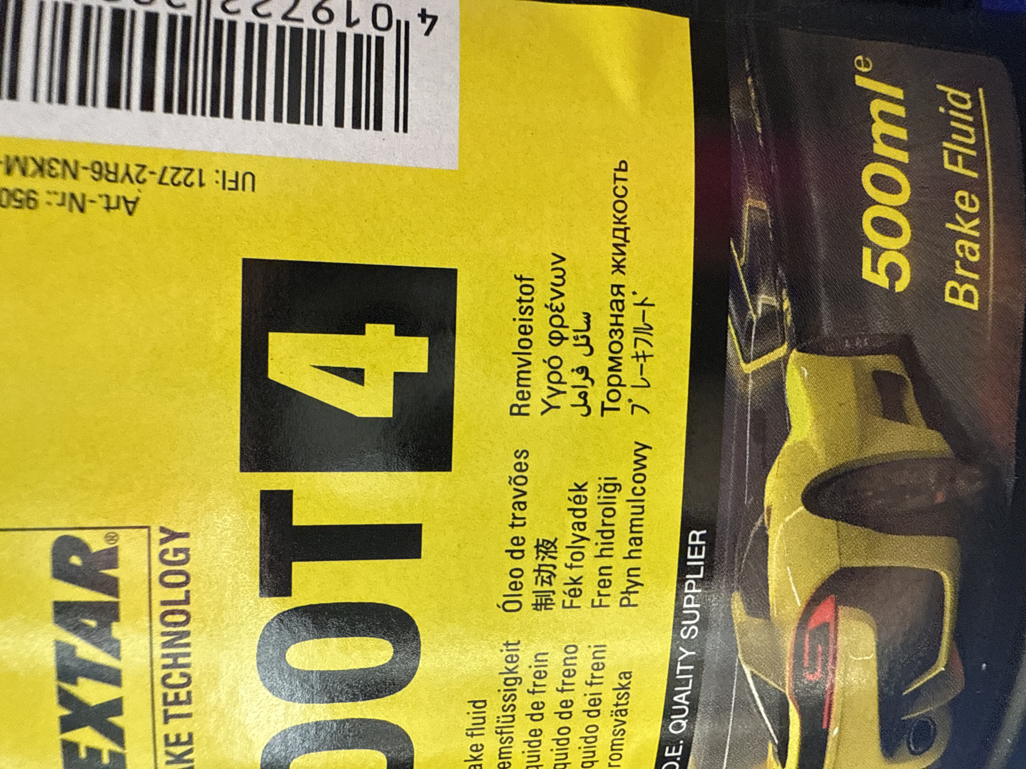 The image shows a close-up of a bottle of "EXTAR" brand DOT 4 brake fluid. The bottle is yellow with black text and a partial image of a yellow car. The text includes the product name, volume (500ml), and translations of "brake fluid" in multiple languages including Russian and Japanese. The text "D.E. QUALITY SUPPLIER" is also visible. There is a barcode and a product number: "Art.-Nr.: 950 UFI: 1227-2YR6-N3KM-". The image provides no information about the location being Votkinsk, Russia.