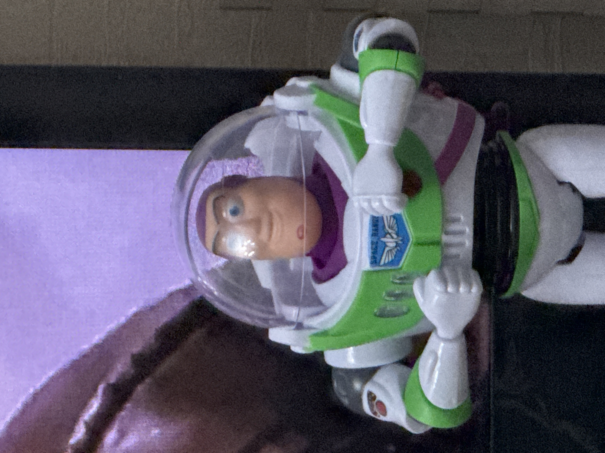 A Buzz Lightyear action figure is positioned in front of a television screen. The background appears to be a room interior. There is no indication of the location being in Tver, Russia.