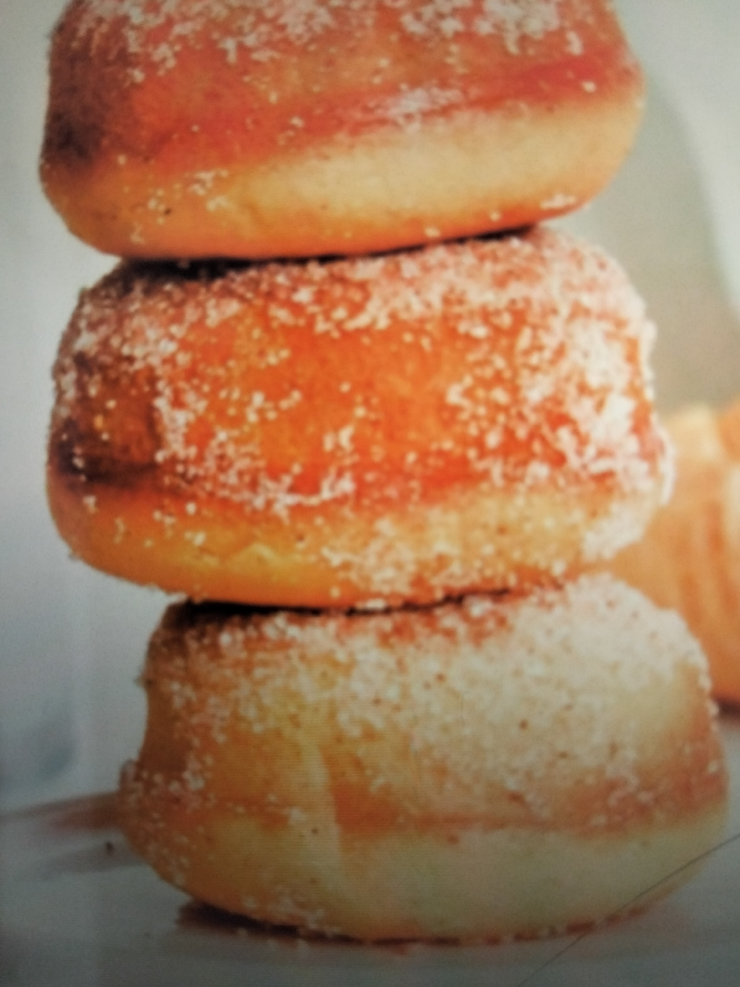 This is a close-up, slightly blurry photograph of three sugar-coated pastries stacked vertically. The pastries appear to be a light golden brown color with a generous coating of granulated white sugar. They are rounded and have a slightly irregular shape. The lighting suggests they are on a flat surface, possibly a plate or table, with a light-colored background that is out of focus. There is no indication of a specific location in Payagaboh, Indonesia.