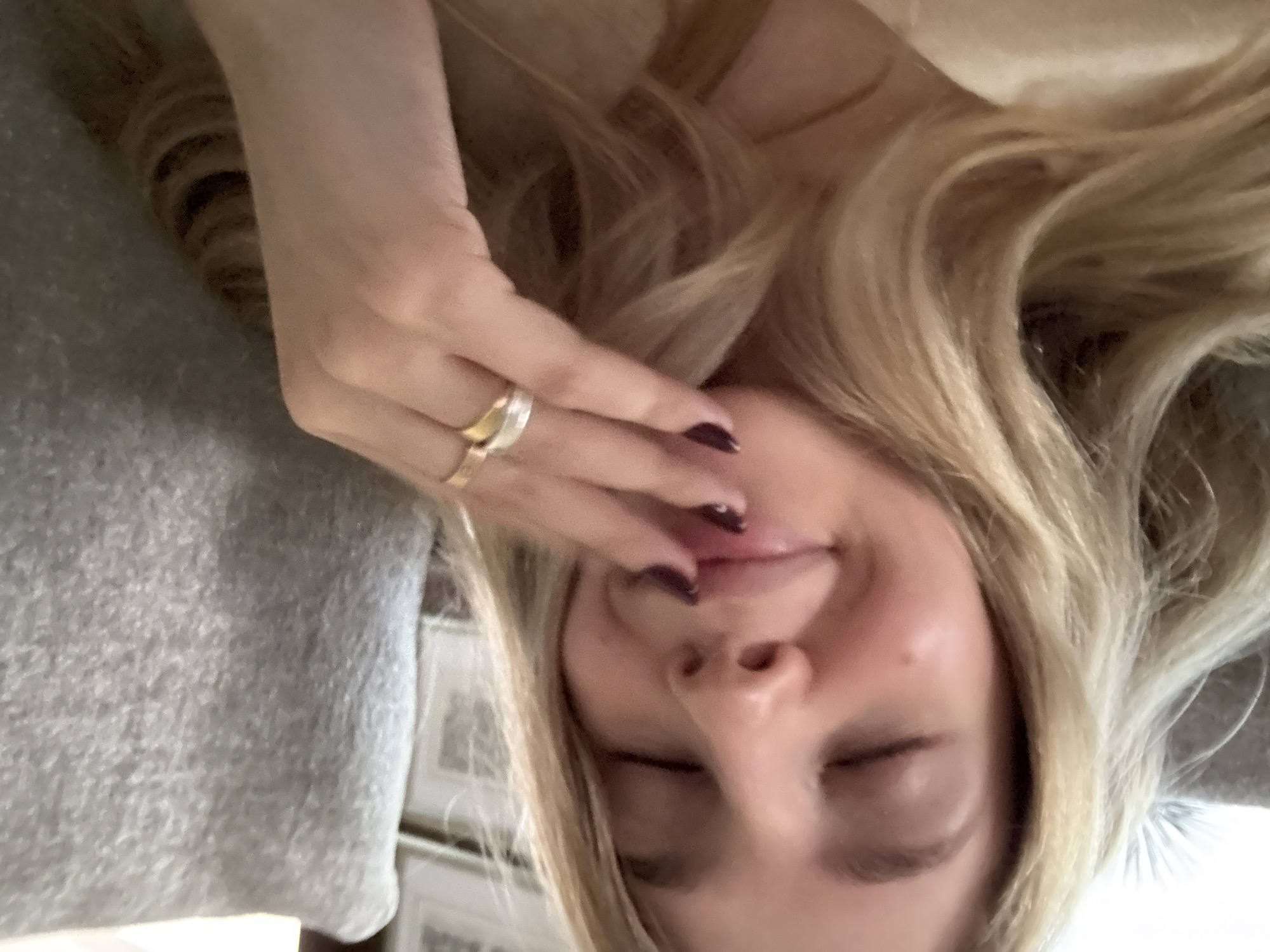 The image shows a woman from a close, upside-down perspective. She has blonde hair and is wearing a ring on her finger. Her eyes are closed, and her hand is near her mouth, touching her lips. A soft, grey surface, possibly a pillow or blanket, is visible in the background. Due to the limited context and lack of landmarks, pinpointing a specific location in Mexico City is not possible.