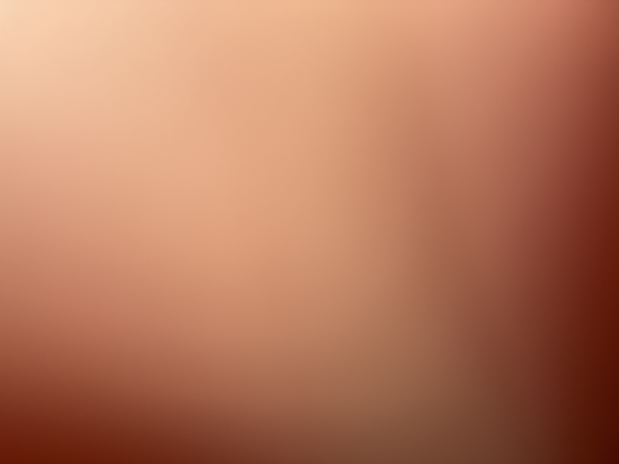 The image is a blurry, abstract composition of warm, gradient tones, transitioning from a dark reddish-brown in the lower left corner to a lighter, peachy-orange hue in the upper right. There are no discernible subjects, objects, people, or actions present. The image appears to be a photographic background or a representation of light diffusion. Its location in Varna, Bulgaria, cannot be determined from the visual information provided.