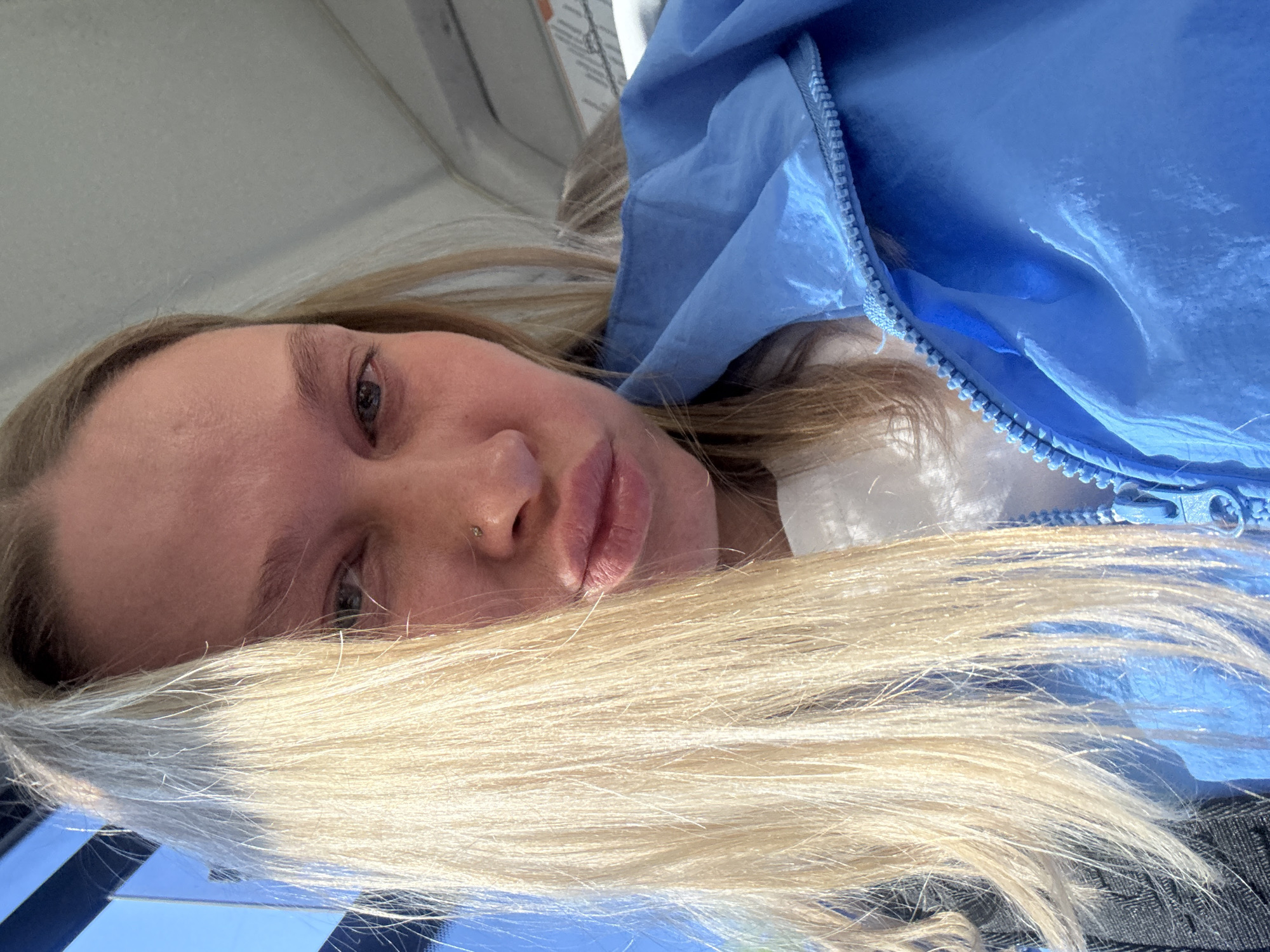A young woman with blond hair and a nose ring is lying down, wearing a blue jacket. The location is possibly Perm, Russia.
