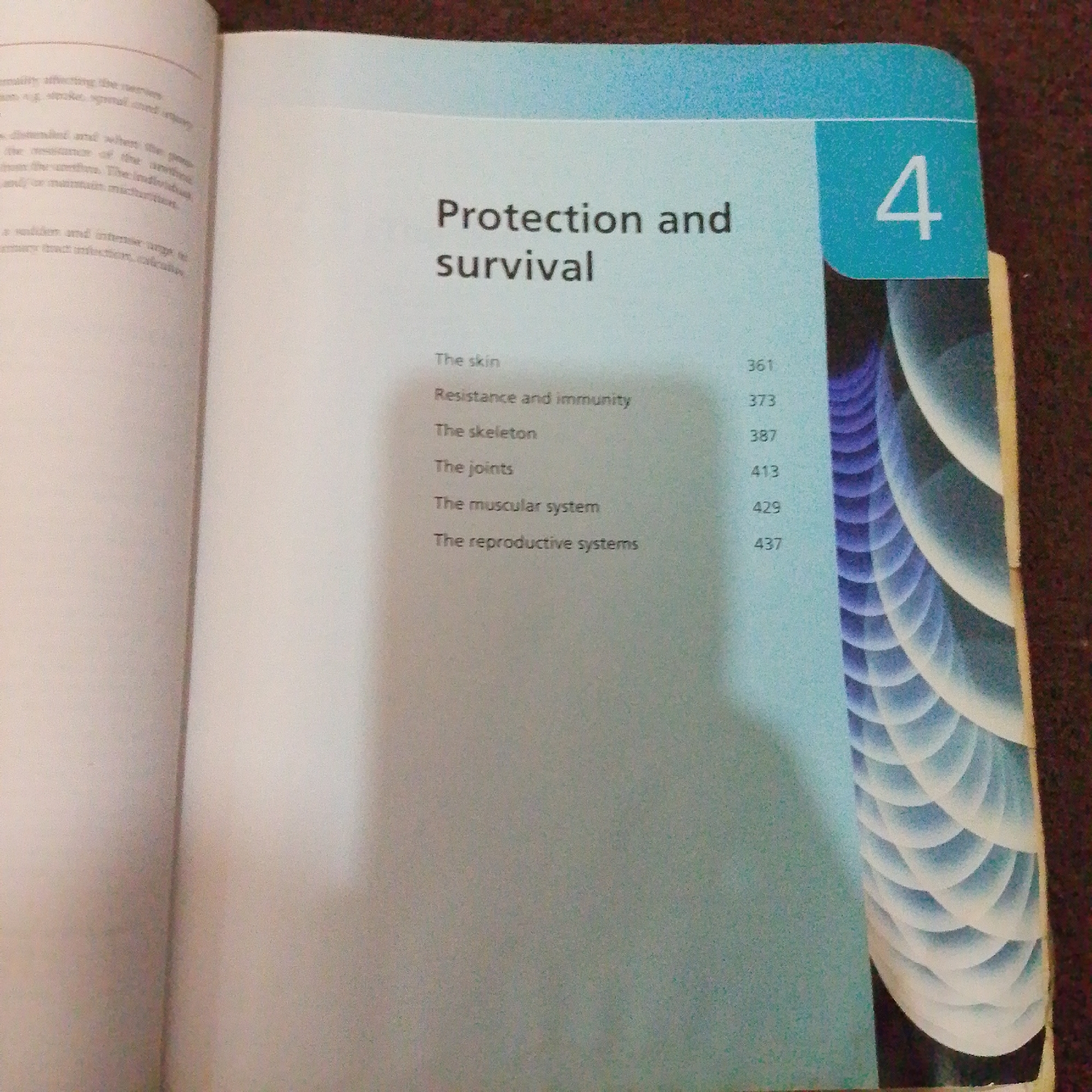 This media file displays an open book, specifically a page from a textbook or reference material. The subject matter is a chapter titled "Protection and survival." The page is divided into two columns. The left column contains a list of subtopics and their corresponding page numbers: "The skin" (361), "Resistance and immunity" (373), "The skeleton" (387), "The joints" (413), "The muscular system" (429), and "The reproductive systems" (437). The right side of the page features a large, stylized number "4" in a blue box, indicating the chapter number. Below the chapter title and subtopics, there is a decorative graphic with a pattern of overlapping curved shapes in shades of blue and white, resembling scales or layered petals. The background of the page is a light blue gradient. The book is resting on a surface that appears to be a dark, textured material, possibly a rug or carpet. The lighting suggests an indoor setting, with no specific time of day or weather conditions indicated. The image is focused on the book, with parts of the surrounding environment slightly blurred. The overall impression is that of an educational or informative context. There is no indication of people or any specific emotional context. The location context of Jalingo, Nigeria is not directly evident from the image itself.
