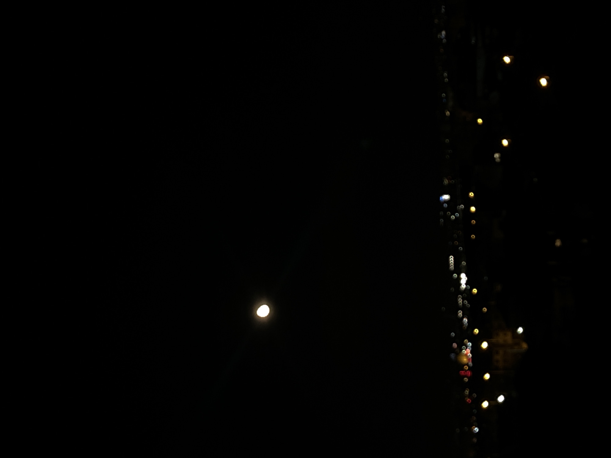 A night scene with a dark background. On the left side is a single, bright moon. On the right, a vertical string of blurred lights suggests city lights. The scene is likely taken from within a building, viewing the cityscape at night. There's not enough information to confirm it's Sofia, Bulgaria. Further details are needed to assess this claim accurately.