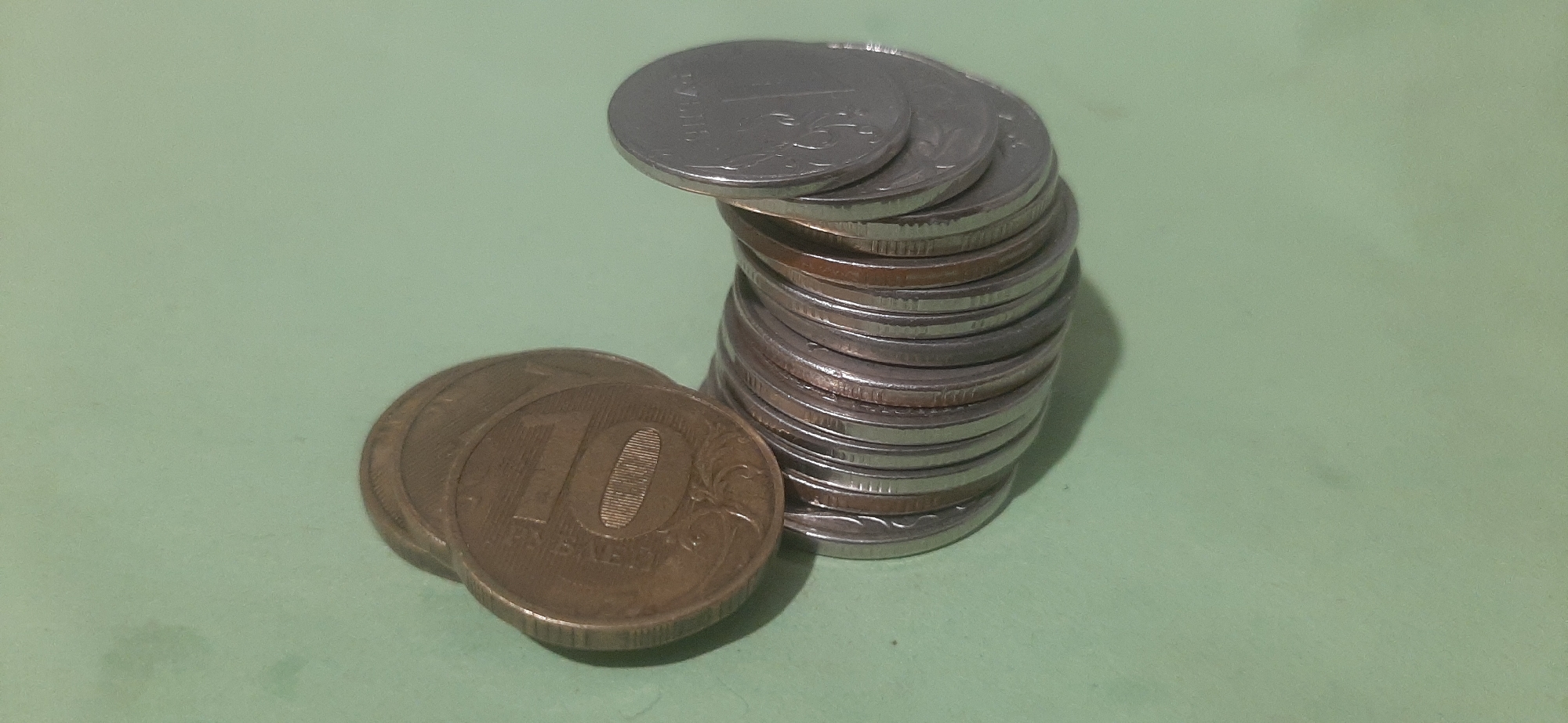 Two stacks of coins are on a light green surface. The stack on the left is made of at least three copper-colored coins, with the top coin displaying the number "10" prominently. The stack on the right is taller and made of silver-colored coins, with one coin at the top displaying the number "1". The image is a close-up shot, with no people or other identifiable objects visible. The location in the city of Yessentukskaya, Russia, is not depicted or implied in the image.