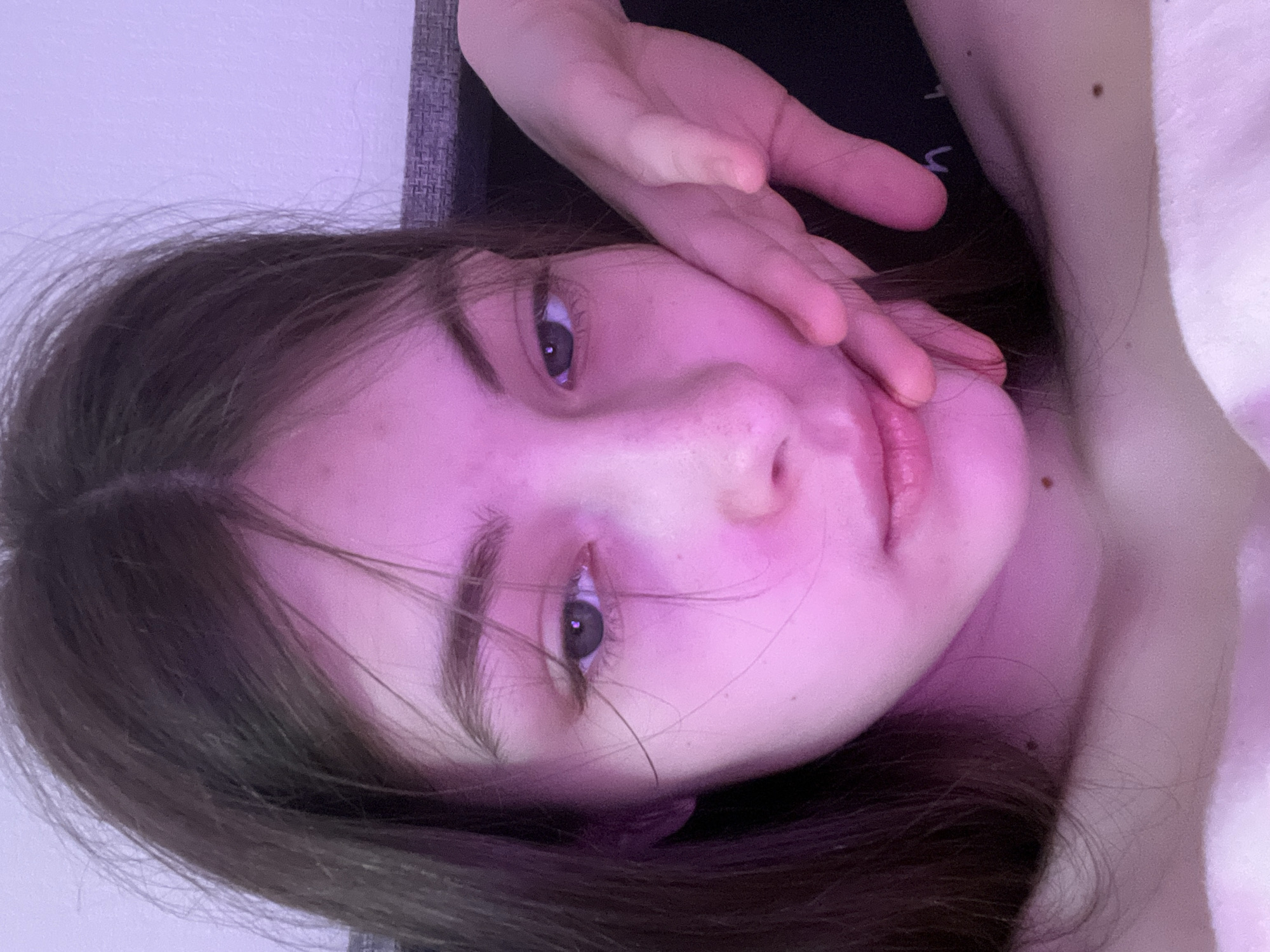 A young woman is lying down, partially obscured by her hand, and illuminated by a pink light. Her hair is brown, and her eyes are visible. There are no indications of location within Saint Petersburg, Russia.