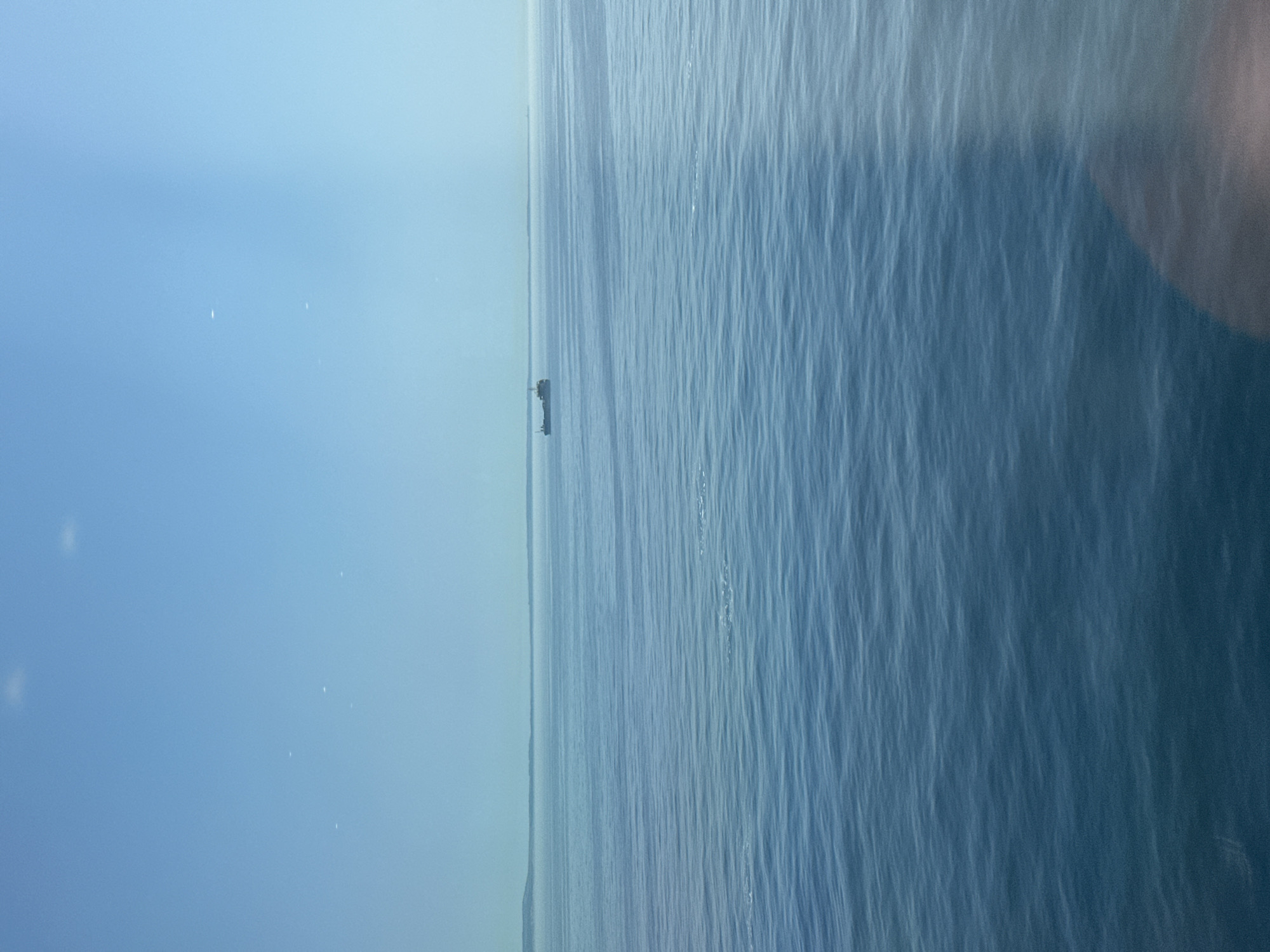 The image shows a body of water, likely the sea, with a small structure visible in the distance. The sky is overcast and blue-gray. The water is choppy, with noticeable wave patterns. The location is unknown, France. No people are visible. The object is the structure in the water, possibly a platform or buoy. No actions or interactions are observable. The environment is marine, with a cloudy sky.