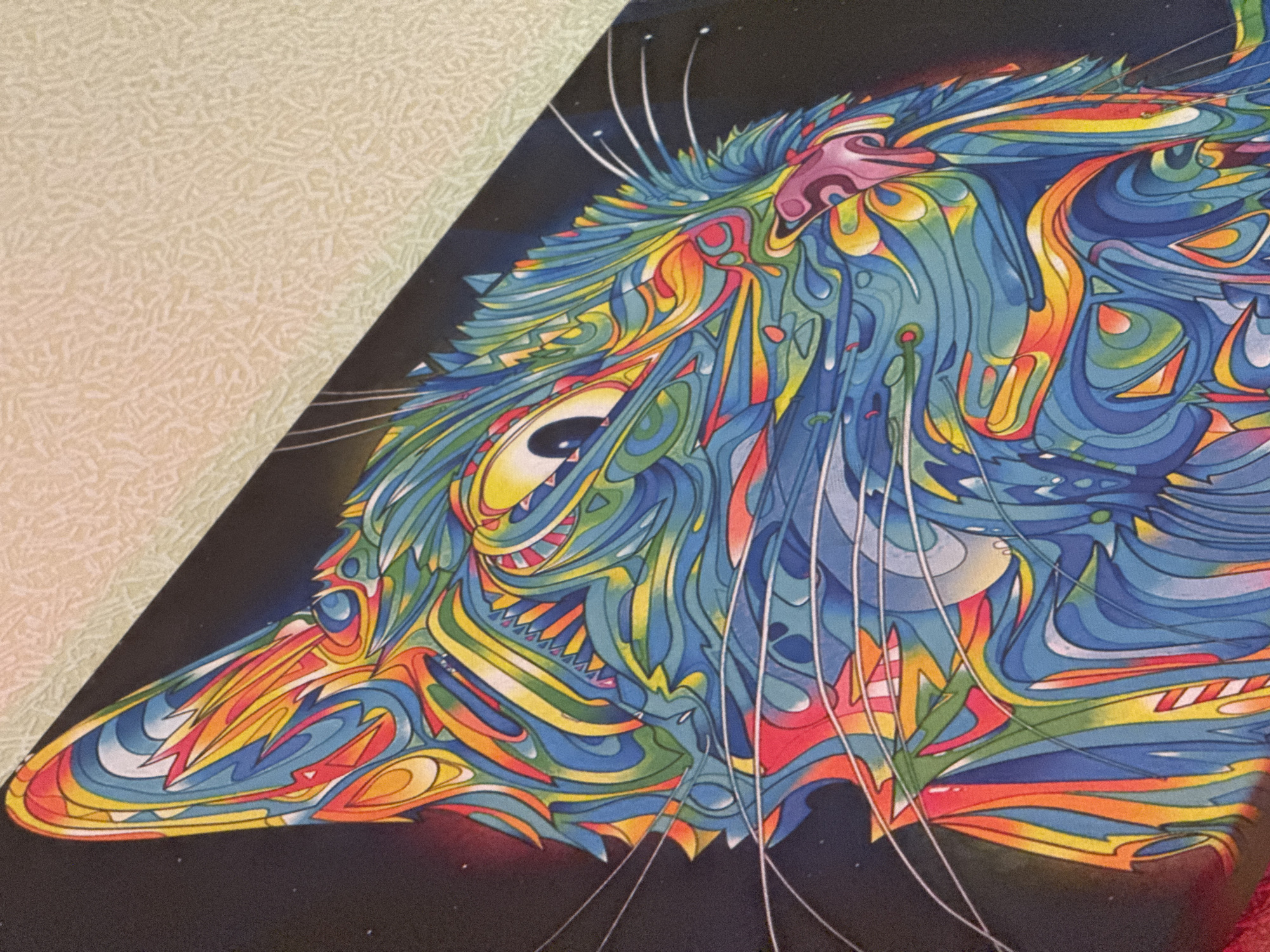 The image shows a brightly colored, stylized depiction of a fox's head. The fox is facing left and occupies most of the right half of the frame, set against a black background. Its fur is represented through swirling, organic shapes rendered in blue, yellow, orange, red, and white. The fox's eye is yellow with a dark pupil. There are thin, white whiskers extending from the fox's face. The left side of the image shows a cream-colored, textured surface. The image is located nowhere in the city of Ново-Никольское, Russia.