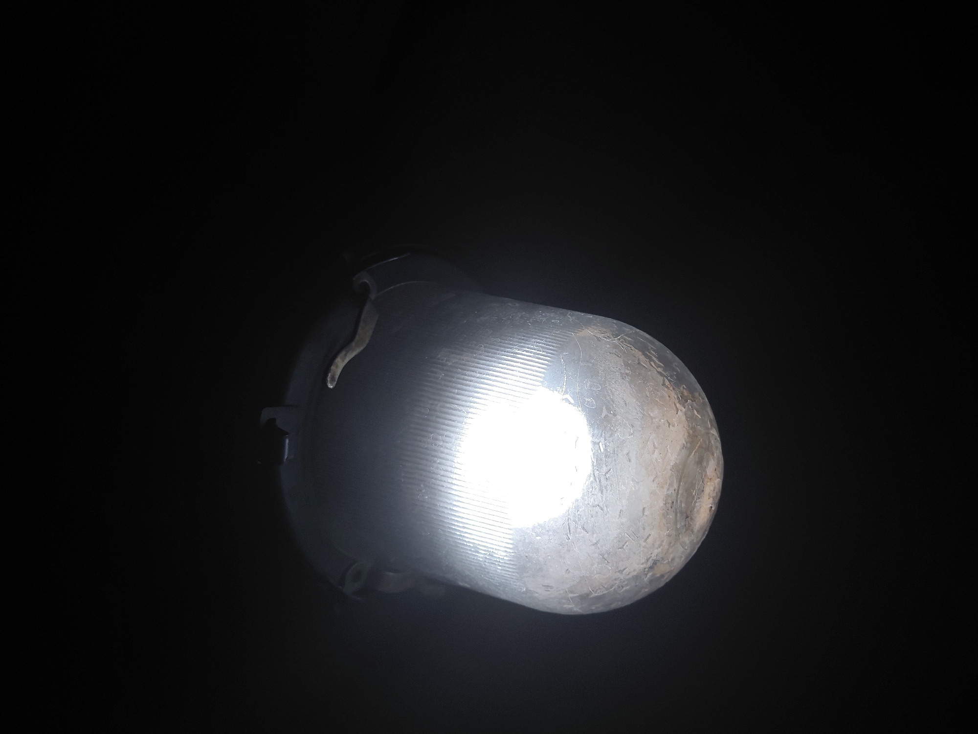 An illuminated bulb with a ribbed surface is situated in the lower center of the frame against a black background. The light emanating from the bulb is concentrated in its center, creating a bright spot. Some structural elements of the bulb's base are visible. The city and location are Unknown, Unknown.