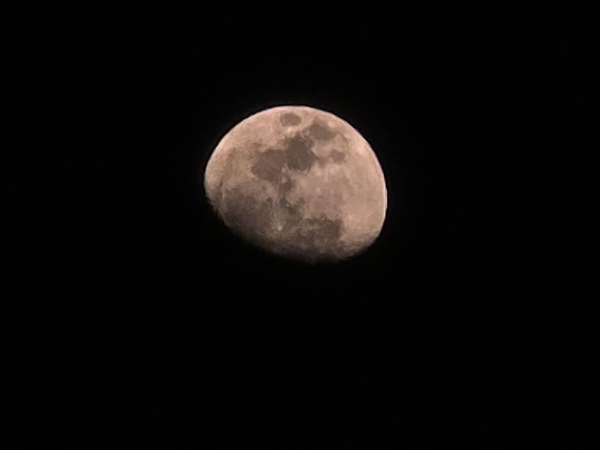 An image shows a close-up of the moon against a black sky. The moon is partially illuminated, with about two-thirds of its surface visible. The visible portion of the moon displays craters and other surface features, appearing in shades of brown and grey. The background is entirely dark, suggesting it is nighttime and there is no visible light pollution. There are no people, buildings, or any other objects in the image. The image does not contain any information about the city of Yambol, Bulgaria.