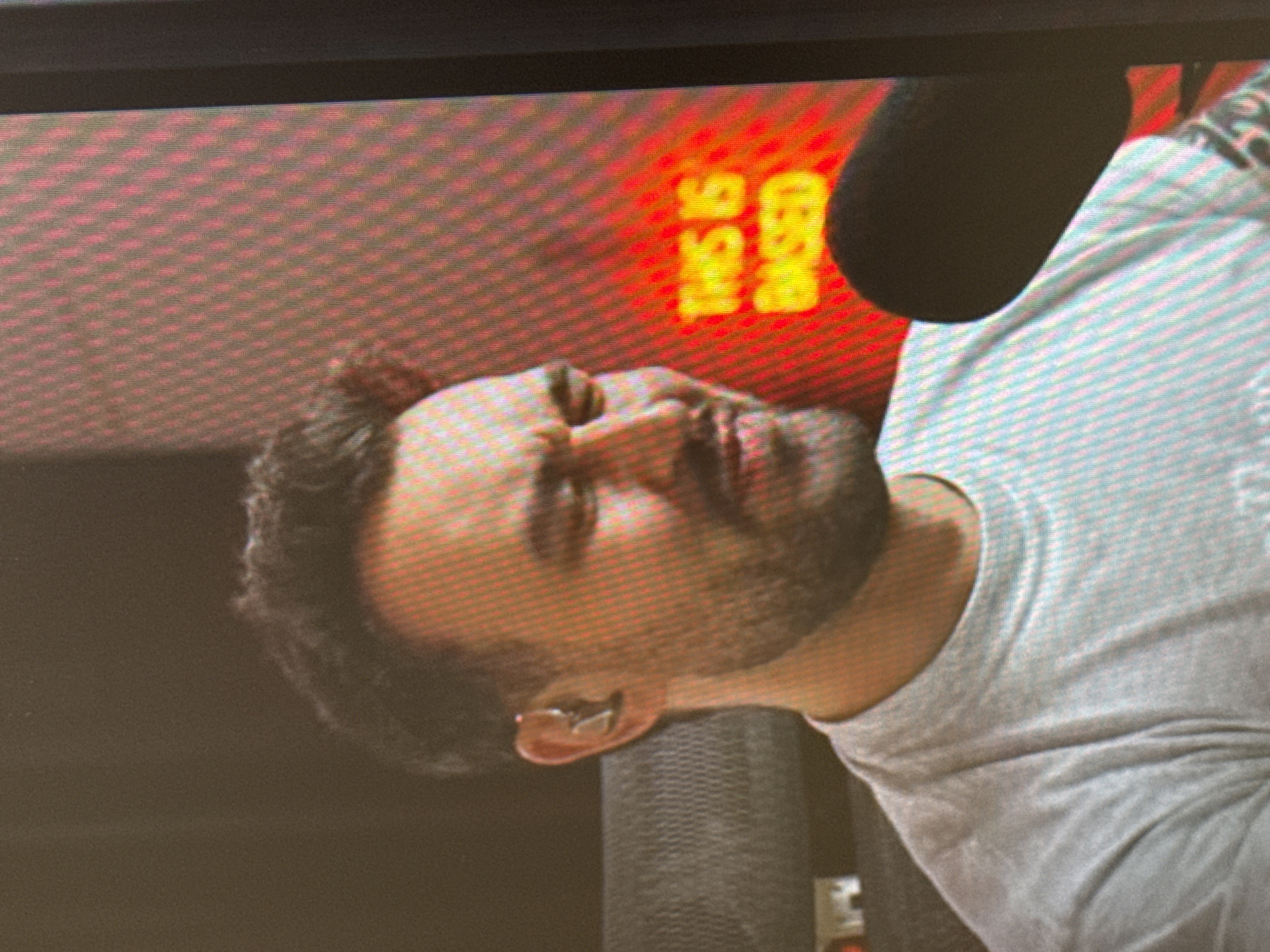 This is a slightly tilted, close-up media file showing a man in the foreground. He has short, dark, curly hair and a beard. He is wearing a light-colored t-shirt. He appears to have an earring in his left ear. His eyes are closed, and his head is tilted back.
In the background, a red, pixelated screen displays yellow text that reads "THIS IS BASED". To the right of the man's head, a dark, rounded object, likely a microphone, is partially visible. The overall setting appears to be indoors, possibly a studio or a broadcast environment, given the screen and microphone. The lighting is warm, predominantly from the red screen, casting a reddish hue on the man's face and neck. The man's expression suggests he might be listening to something, resting, or perhaps in the middle of a performance or recording. There are no clear indications of time of day or weather. The location context is provided as Saratov, Russia.