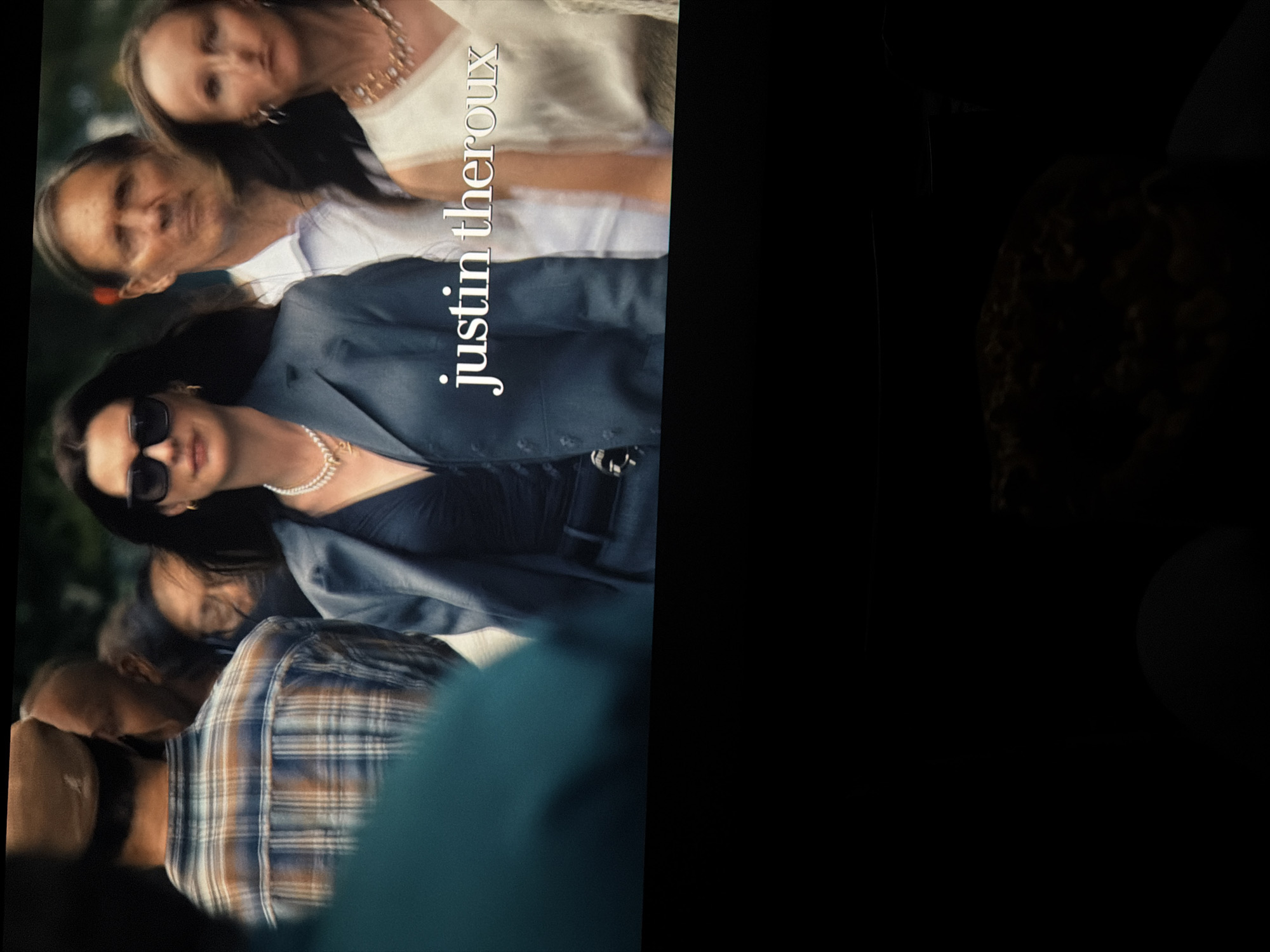 The image shows a group of people, with "justin theroux" overlaid in white text. There are at least six individuals, positioned closely together. One woman wears sunglasses and a dark suit with a pearl necklace. Above her, two older women are visible, one with a white top and necklace. Below the woman in sunglasses, a person in a plaid shirt is partially visible. The right portion of the image is predominantly black, with indistinct shapes suggesting obscured objects. The location is not apparent and there is no evidence it is in Kaiserslautern, Germany.