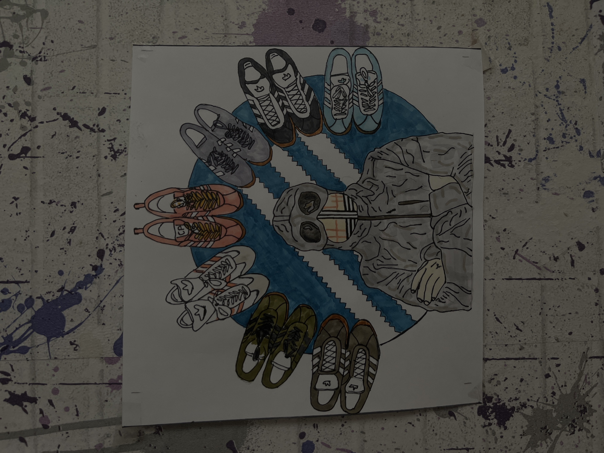An illustration on a piece of paper is affixed to a wall with paint splatters. The illustration depicts a circle of various Adidas shoe designs surrounding a stylized figure wearing a garment with goggles over their face, centered over a blue representation of the Adidas stripes. The setting appears to be indoors, on a wall with a textured, mottled surface. There is no indication of Maladzyechna, Belarus.