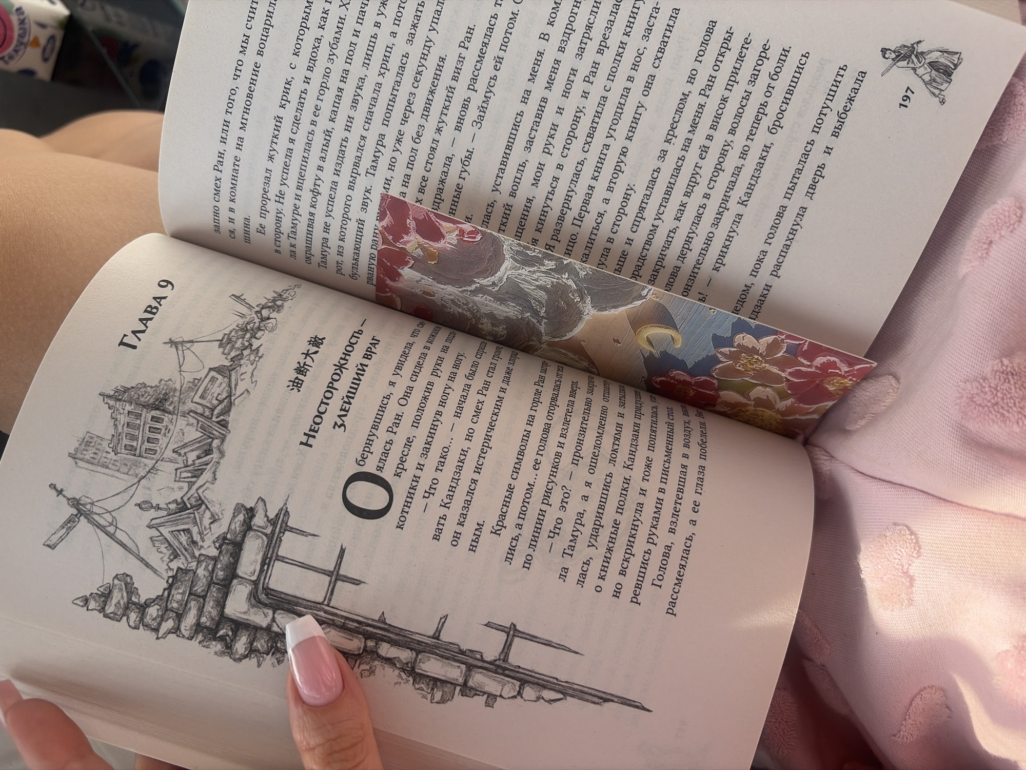 A person is holding open a book, displaying two pages with text in Russian and an illustration of a dilapidated building, possibly a ruin. The open book reveals what appears to be the beginning of a chapter with the title "ГЛАВА 9" (Chapter 9). A bookmark is placed within the book. The pages also contain a smaller illustration of a person, and the number "197" is printed at the bottom right. The image suggests someone is reading or has been reading the book. The context points to a narrative centered around a story, as evidenced by the chapter heading and book number. The surroundings are soft and blurry, suggesting a personal and relaxed setting for reading. The person's hand is visible, showing manicured nails. There are no elements suggesting that the image was captured in St. Petersburg.