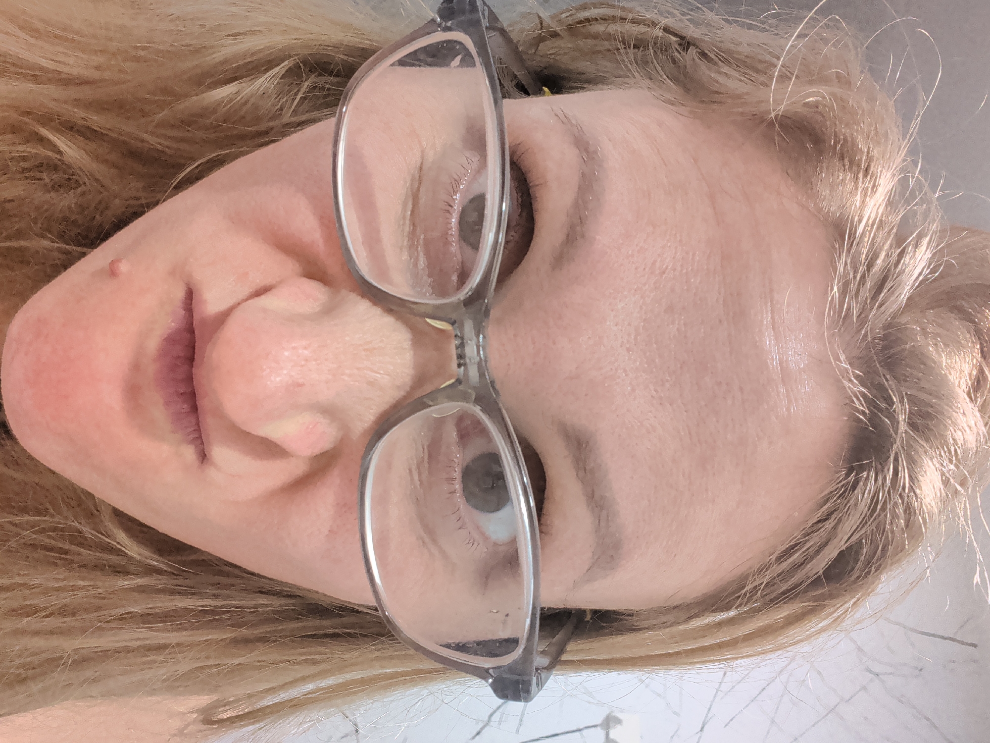 A close-up, rotated view of a blonde woman's face wearing glasses. The background is ambiguous. There is no evidence that this image was taken in Ko Pha-ngan, Thailand.