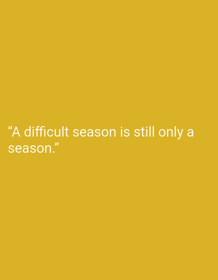 The image is a vertical, full-frame, close-up shot against a solid, muted yellow background. White text is centered on the left side of the frame. The text reads: "A difficult season is still only a season." There are no people, objects, or environmental elements present in the image, nor is there any indication of the city of Magelang, Indonesia.