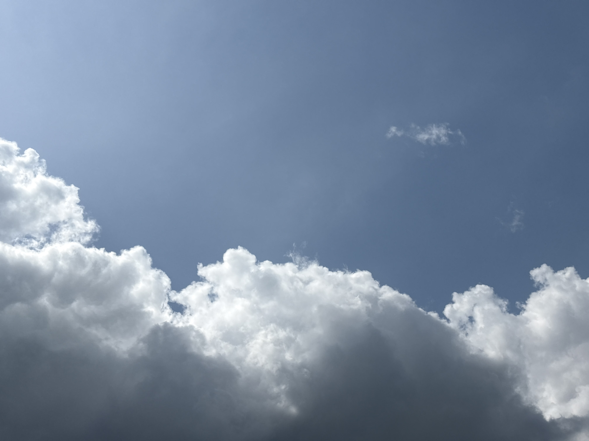 The image shows a cloudy sky. The lower portion of the image is dominated by a dense layer of cumulus clouds, with varying shades of gray and white. The upper portion reveals a blue sky with a small, isolated cloud formation. No people, subjects, or objects are discernible that would indicate a specific location in Ikot Ekpene, Nigeria or any other identifiable city.