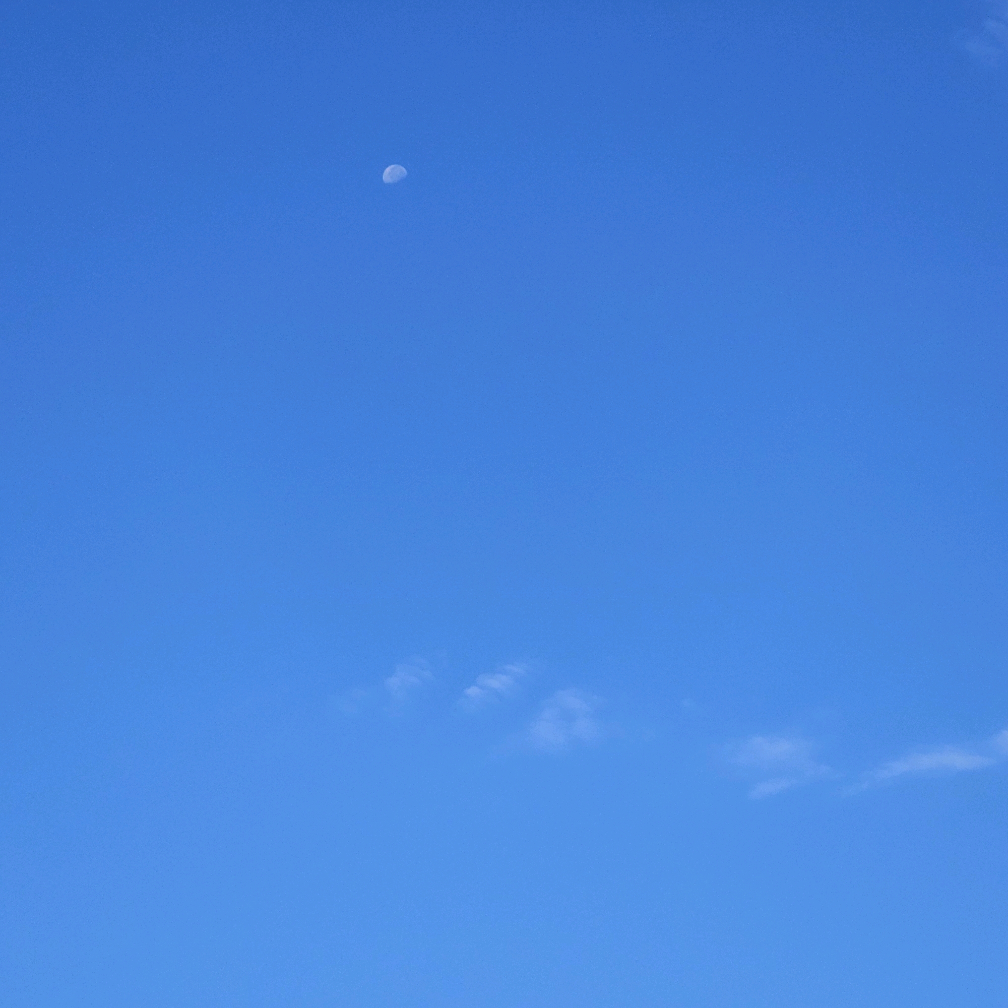 The image depicts a clear blue sky with a visible moon in the upper left quadrant. There are a few wispy clouds scattered across the sky, predominantly in the lower portion of the image. The scene appears to be an outdoor shot, likely taken during the daytime as indicated by the bright sky and the visibility of the moon. No specific landmarks or elements within Ventimiglia, Italy are discernible in this image.