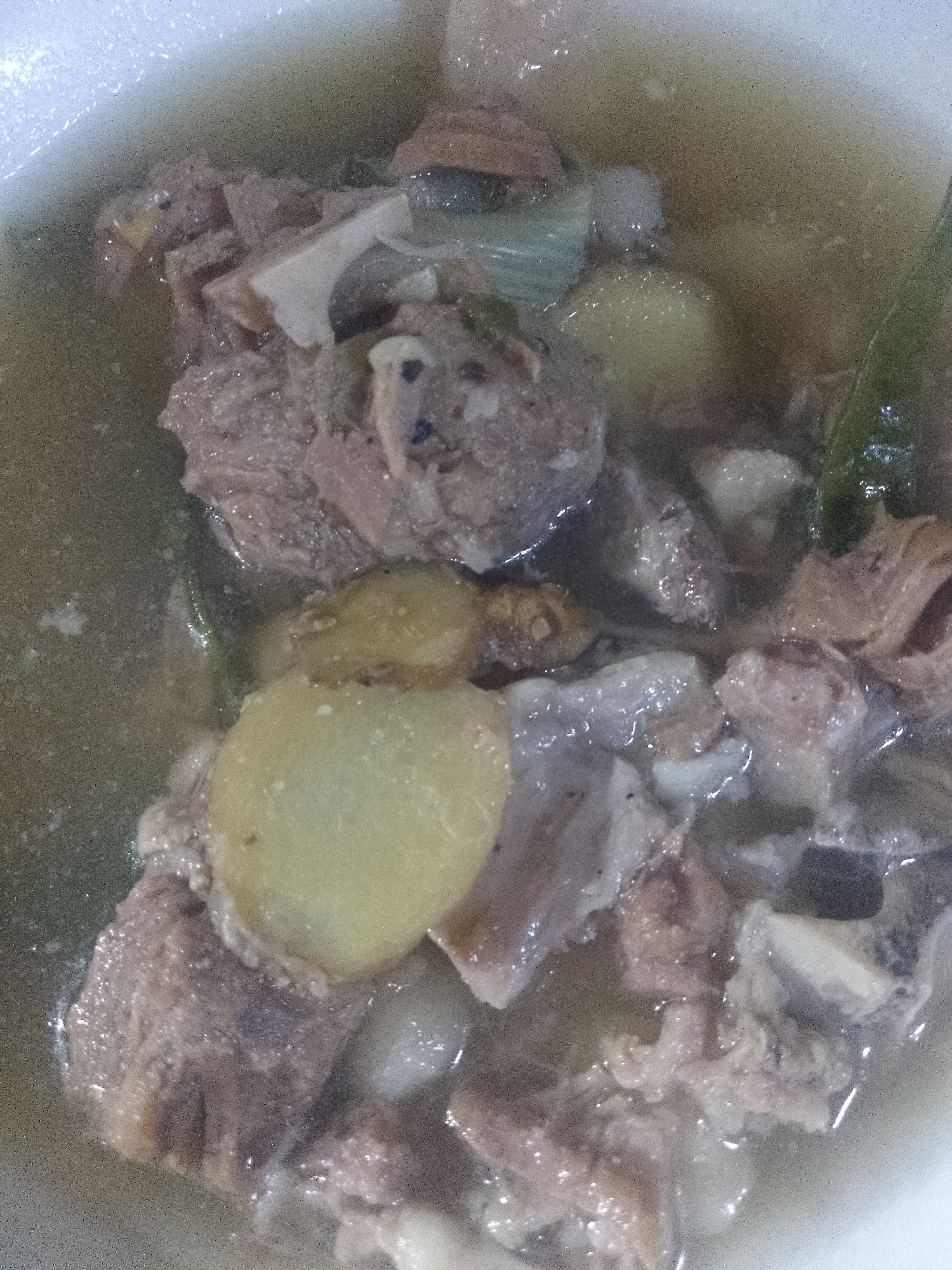 A close-up shot depicts a bowl of Nilaga, a Filipino soup, with visible pork ribs, potato slices, green leafy vegetables, and other ingredients simmering in a broth. The setting is likely a kitchen or dining area in Davao City, Philippines. The focus is on the food itself, with the details of the dish being prominent.