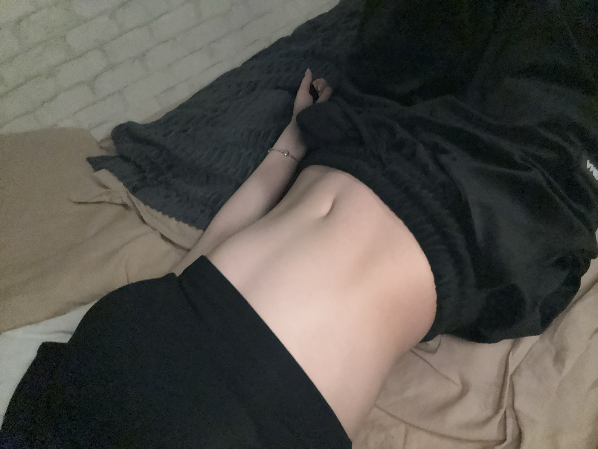 A person is lying on a bed. The person has a visible torso and arms. The person is wearing black shorts. A black blanket covers part of the torso and head. The location is not discernible.