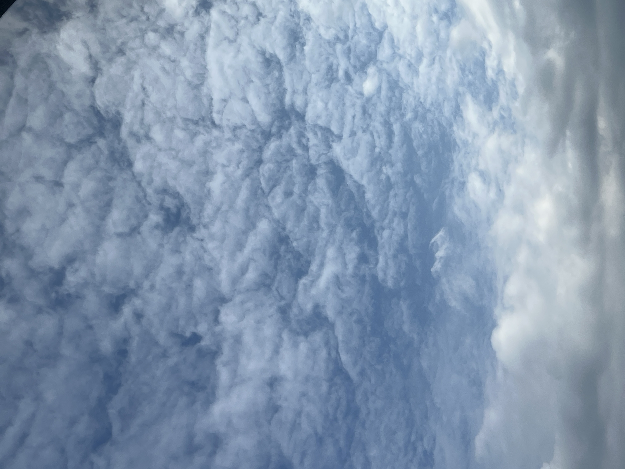 The image shows a sky with clouds. The clouds are a mix of white and gray, with some blue sky visible between them. The clouds appear to be of various types, including cumulus and stratus clouds. The image is taken from a low angle, looking up at the sky. There are no visible landmarks or features that would indicate the location in Warsaw, Poland.
