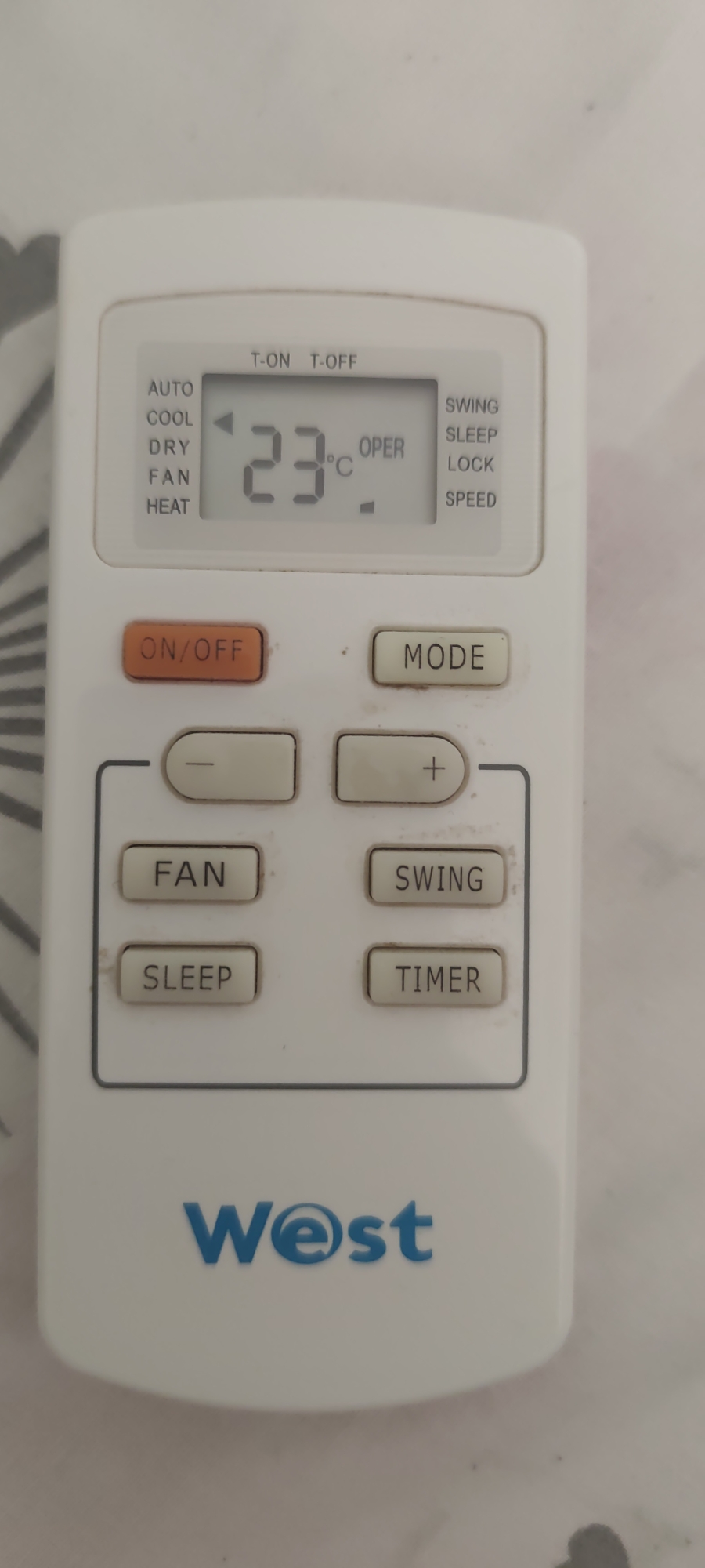 The image shows a white air conditioner remote control. The remote has a digital display showing "23°C" and "OPER". Below the display are several buttons, including "ON/OFF", "MODE", "-", "+", "FAN", "SLEEP", "SWING", and "TIMER". The brand name "West" is visible at the bottom of the remote. The background is a light-colored, textured surface, possibly a wall or furniture. There are no people or any context about the location in Kyiv, Ukraine.