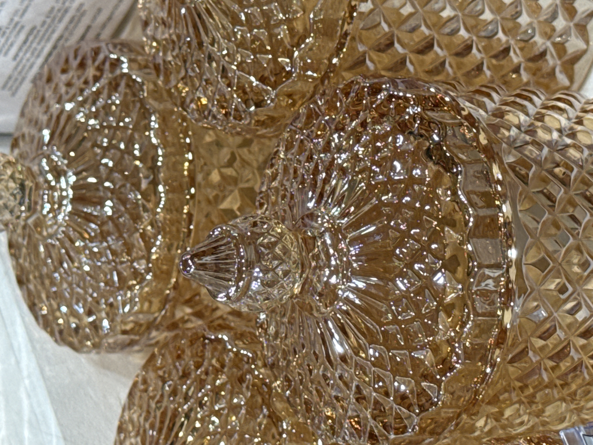 The image shows a close-up of several decorative amber-colored glass ornaments. The ornaments are spherical with a textured, faceted surface that creates a sparkling effect. Some ornaments have a pointed, bulbous top. The background is blurred, but appears to be a light-colored surface. The image's details indicate indoor setting and decorative object photography. Given the lack of specific information such as street signs, famous landmarks, identifiable buildings, and people wearing culturally specific attire, it is impossible to definitively locate this image in Saint Petersburg, Russia. The details provided can't connect it to the specified city.