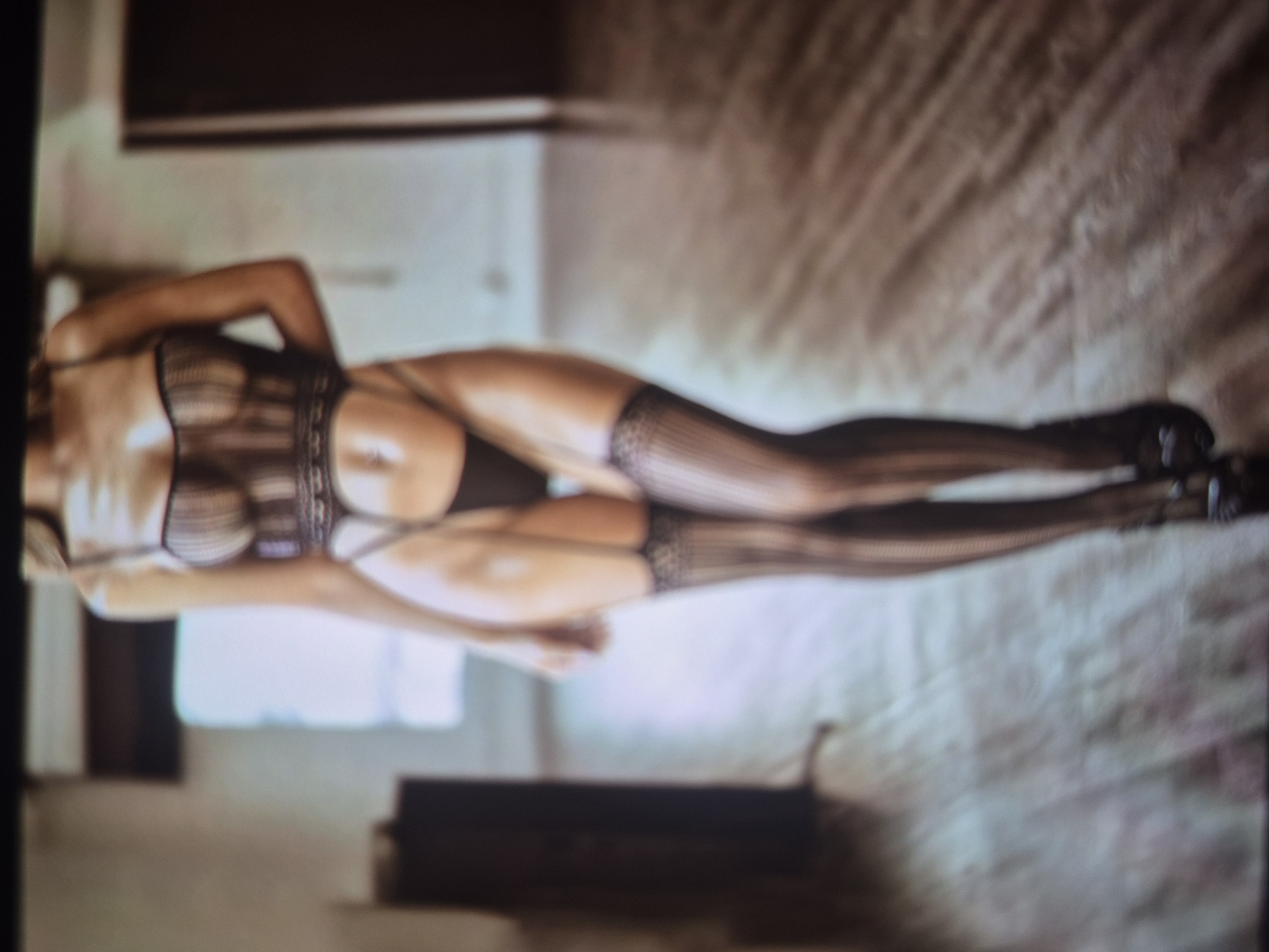 A woman in black lingerie and stockings lies on a bed. The setting is an interior, possibly a bedroom. It is not possible to determine the location in Tbilisi, Georgia.