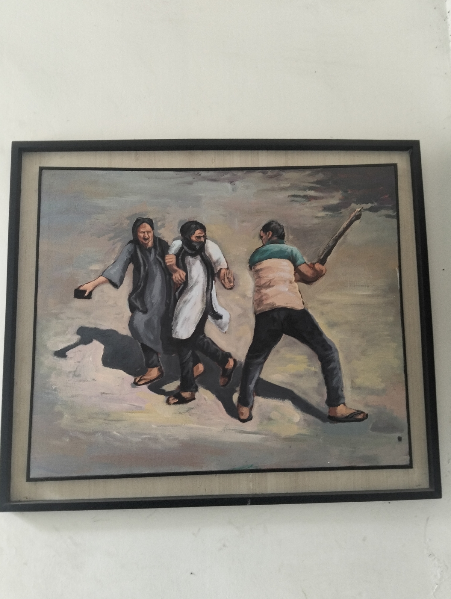 The image is a framed painting depicting a scene of violence. Two people are being pursued by another person wielding a club or stick. The person being pursued on the left is holding a dark, rectangular object. All three figures are wearing sandals. The background is a neutral, possibly urban environment with muted colors. There are no definitive markers to identify the specific location as Dhaka, Bangladesh.