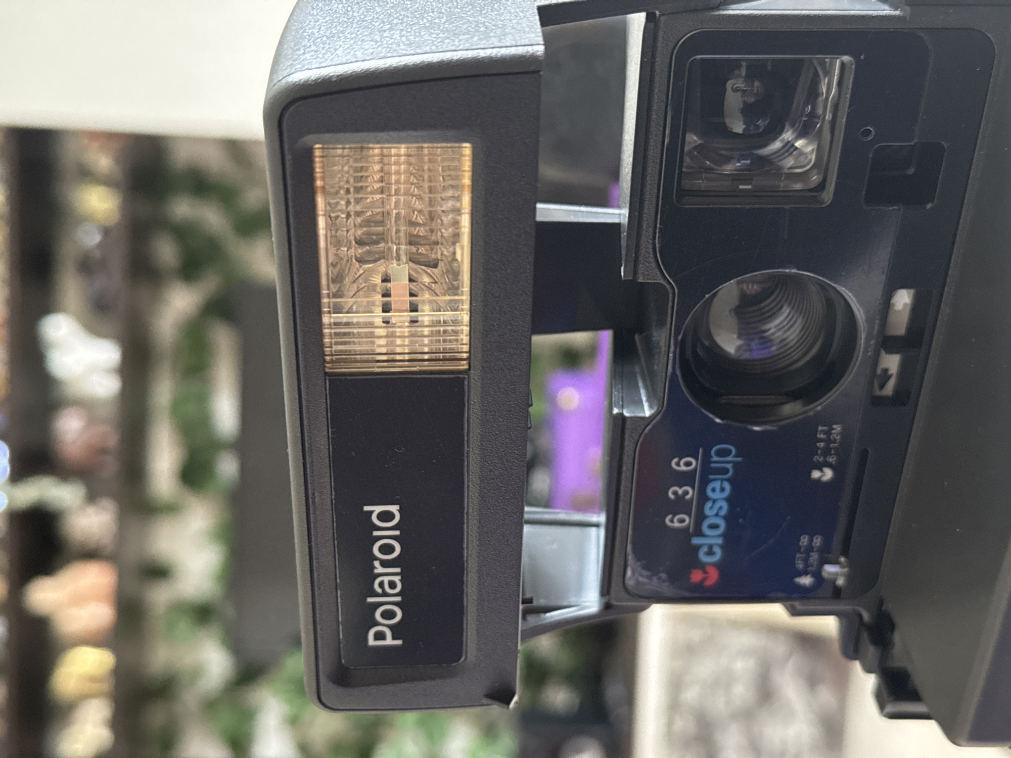 A close-up shot of a Polaroid 636 Closeup instant camera. The camera is black and features the Polaroid logo on the flash unit. The lens and viewfinder are visible. The camera's "closeup" setting is indicated, along with distance markings in feet and meters. The location is not identifiable from the image.