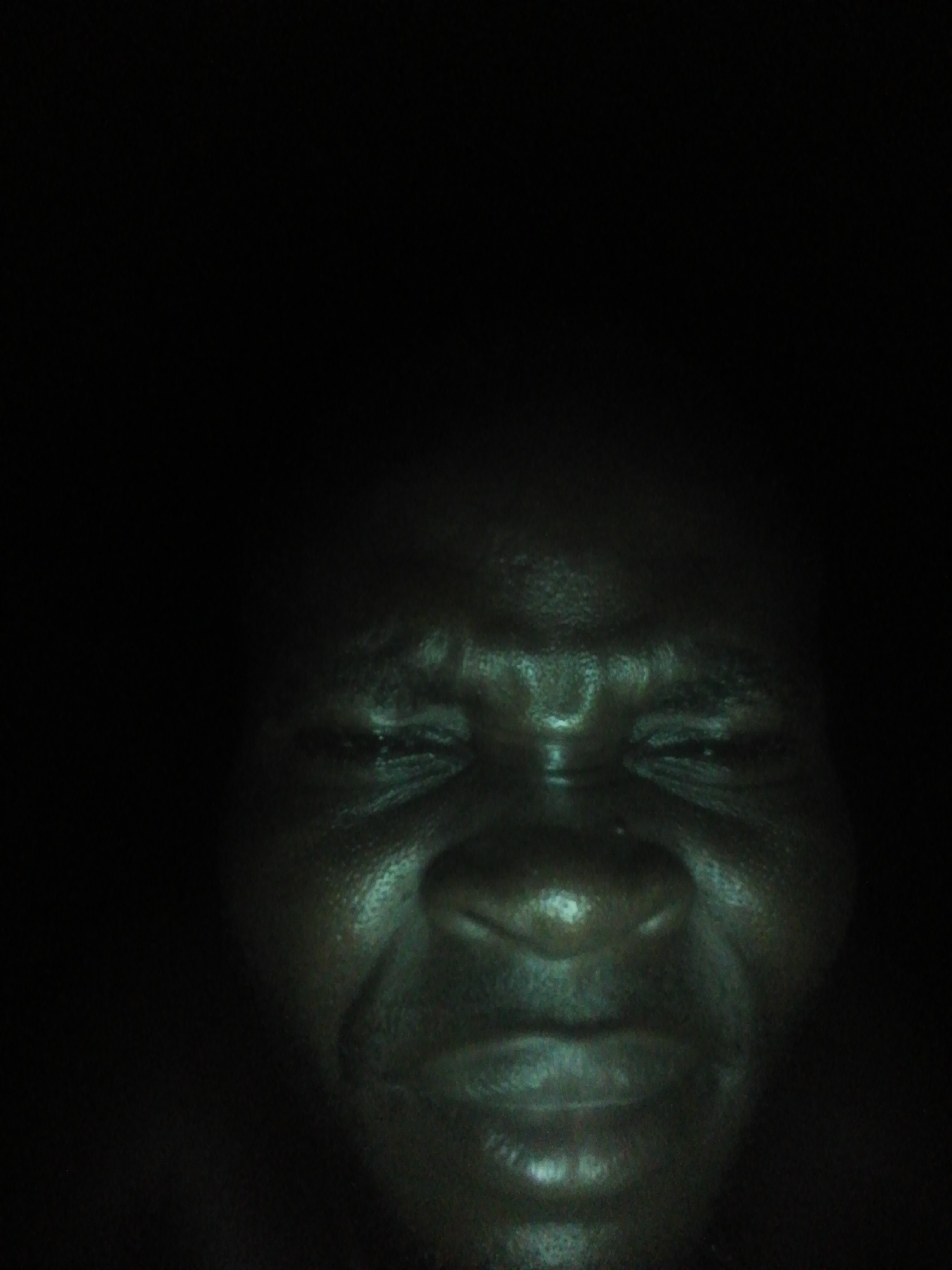 A close-up photograph of a dark-skinned person's face against a stark black background. The face is the primary subject, and the details of the facial features are visible despite the low lighting. No specific elements indicate the location of Ikorodu, Nigeria.
