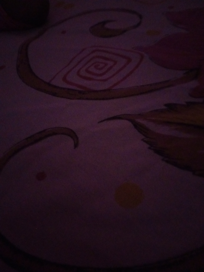 The image shows a close-up of a purple bedsheet with a floral design. The bedsheet is covered in a swirling pattern of pink and yellow flowers and leaves. The image is taken from an angle, and the bedsheet appears to be lying flat on a bed. The image was likely taken in a bedroom in Sambalpur, India. The coordinates given, 21.468, 83.994, are within the city of Sambalpur. There are no people or other objects present in the image. The lighting is dim and the bedsheet appears to be soft. There is a hint of yellow color near the bottom right corner of the bedsheet. The image is a close-up shot of the bedsheet, which is the main subject. The image is clear and well-focused.