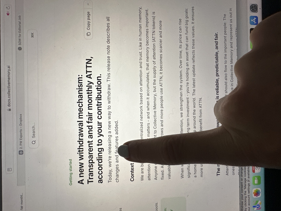 The image displays a close-up, eye-level view of a digital screen, likely a laptop or tablet, showing a web page in a browser. The screen prominently features text with the heading "A new withdrawal mechanism: Transparent and fair monthly ATTN, according to your contribution." Below the heading, the text "Today, we're releasing a new way to withdraw. This release note describes all changes and features added." is visible. The URL `docs.collectivememory.ai` is present in the browser's address bar. Other visible browser tabs include "2. PW Exports - Dropbox" and "SOW for Editorial Job." A human left hand, with pale skin, is positioned in the lower-middle section of the image, with its index finger extended and pointing directly at the word "features" within the sentence "features added." The index finger's nail is painted with a light blue-grey polish. A portion of the thumb and palm is also visible below the index finger. The lower edge of the screen reveals a macOS dock with various application icons. The physical location within the city of Wealden, United Kingdom, cannot be determined from the visual information provided in the image. The scene is indoors.