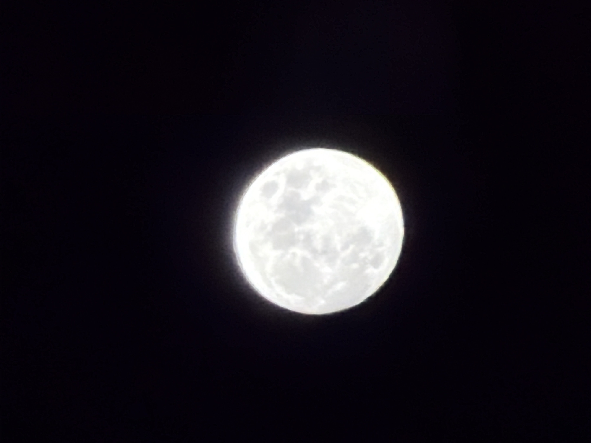 A full moon is centered in the frame against a black background. The moon's surface is visible with varying shades of white suggesting texture and craters. There are no people or identifiable objects apart from the moon and the sky. The location cannot be determined as there are no identifying features.