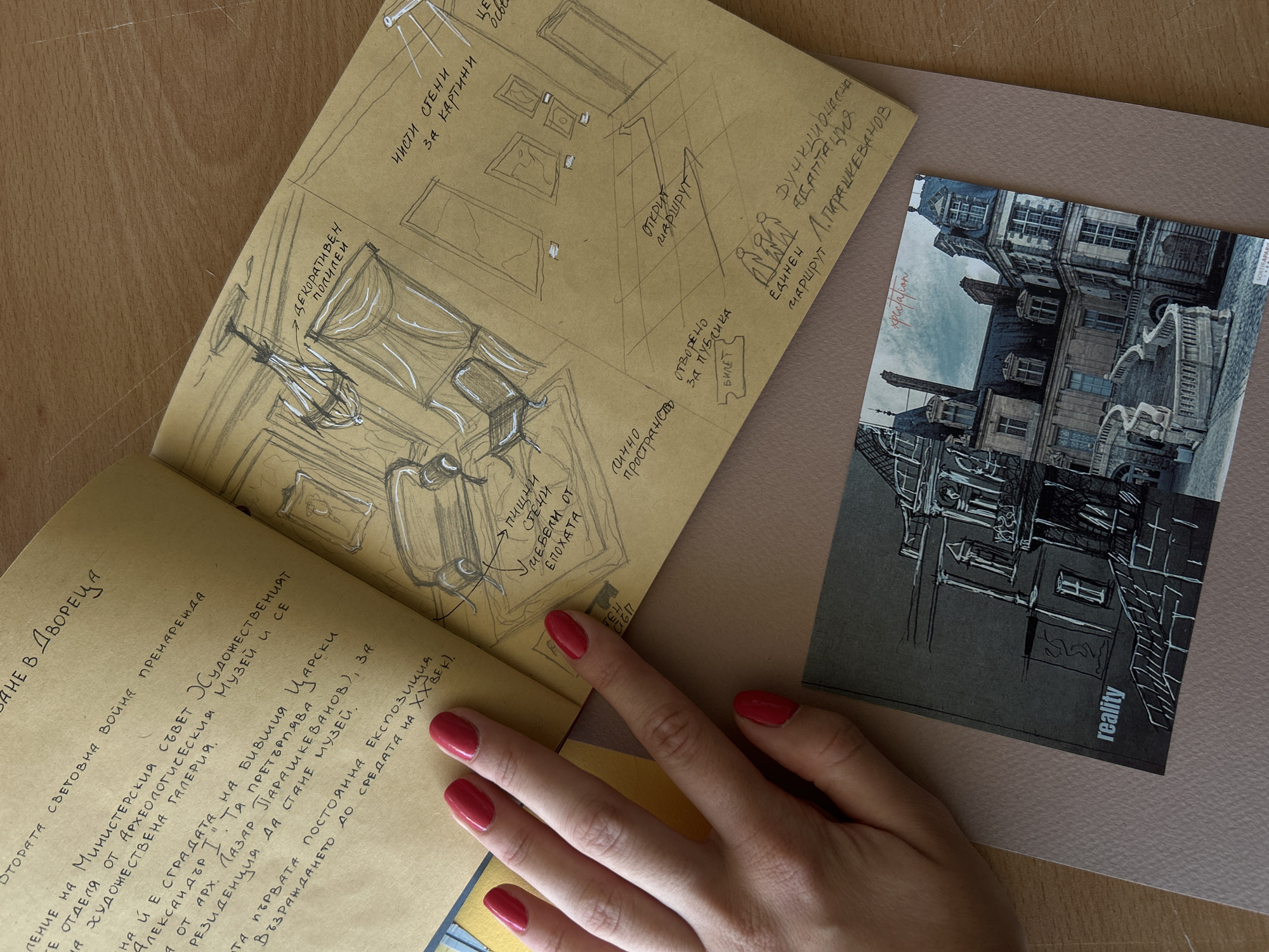 The image shows an open notebook with handwritten text and sketches on a light brown, textured paper. The notebook is placed on a darker brown surface, possibly a desk. To the left, a hand with bright red nail polish is resting on the notebook, partially obscuring some of the text. The text on the left page is in Cyrillic script and appears to be historical or architectural notes, referencing "Министерския съвет," "Археологическия музей," "Царски," "Александър I," and "Парашкеванов." It also mentions "Първата постоянна експозиция" and "възраждането до средата на ХХ век."
The right page of the notebook contains a sketch of an interior space, possibly a room in a palace or museum. The sketch includes furniture like a sofa and chairs, a chandelier, and what appear to be framed pictures on the walls. Labels in Cyrillic script point to different elements of the sketch, such as "декоративен таван" (decorative ceiling), "пищни мебели от епохата" (lush furniture from the era), "чисти стени за картини" (clear walls for paintings), and "открит маршрут" (open route). There are also small figures drawn, labeled as "единен маршрут" (unified route) and "функционална адаптация" (functional adaptation).
In the lower part of the image, a postcard-like item is partially visible. It features a detailed sketch of an ornate building with a grand staircase, possibly a chateau or palace. The word "reality" is printed on the bottom left of this item.
The overall scene suggests a creative or research-oriented workspace, with the notebook and sketches indicating an interest in history, architecture, or museum design, potentially related to a specific location in Sofia, Bulgaria, given the text's references.