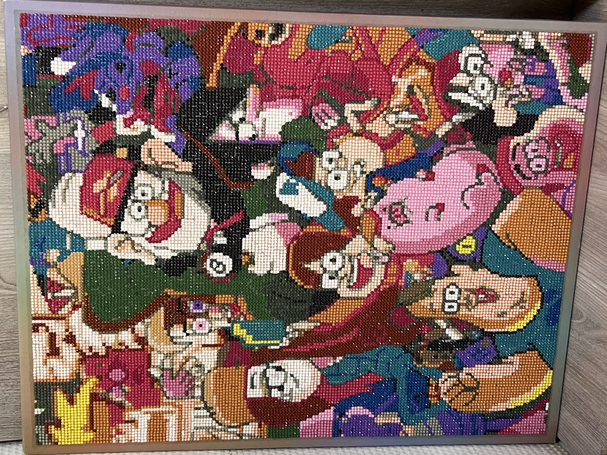 The image shows a framed diamond painting of various characters from the animated television show Gravity Falls. The painting includes Dipper and Mabel Pines, Grunkle Stan, Wendy Corduroy, Soos Ramirez, Waddles the pig, Bill Cipher, and other characters, depicted in a collage style. The diamond painting is framed in a metallic silver frame and appears to be resting on a wooden surface. There is no indication of the location being Chaikovsky, Russia.