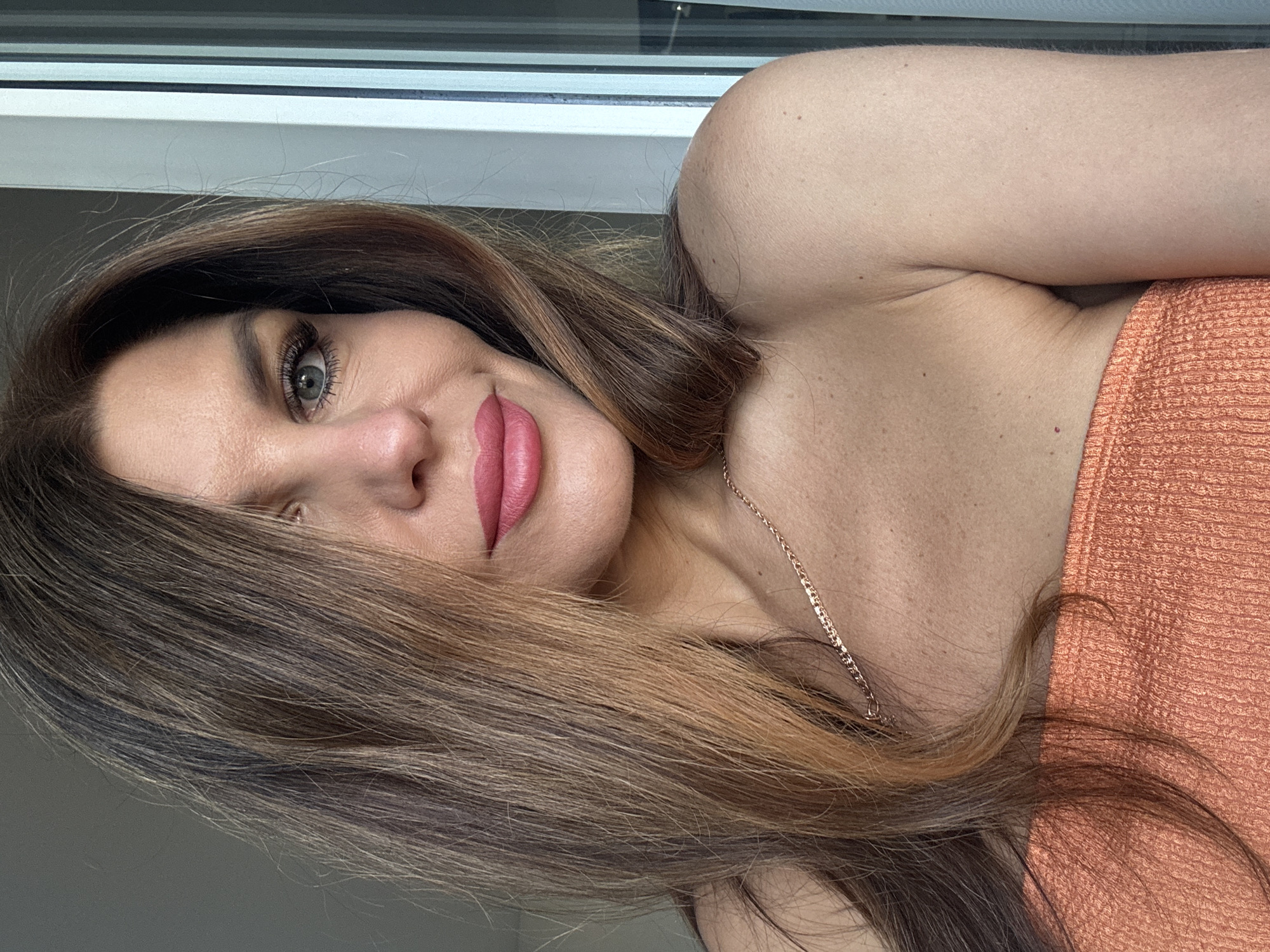 A portrait of a woman with light skin, brown hair, and pink lipstick, taken indoors in a room with a window. No information is available in the image to determine the location in the city of Chaikovsky, Russia.