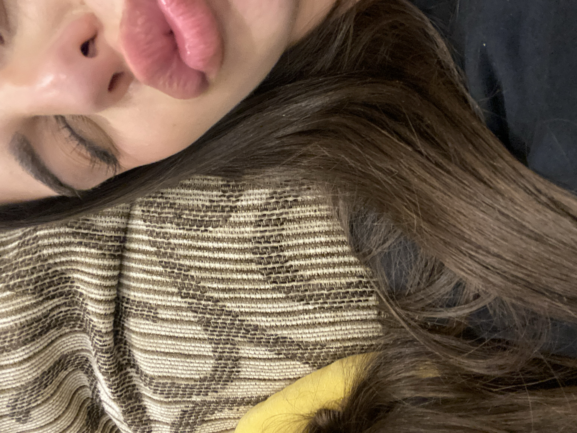 The image shows a close-up of a person's face. The individual is lying down with their head resting on a patterned fabric. Part of their brown hair is visible, as is a portion of their face including a closed eye, nose, and lips. A dark fabric is also visible in the background. There is no information to suggest that this photo was taken in Dragovishtitsa, Bulgaria.