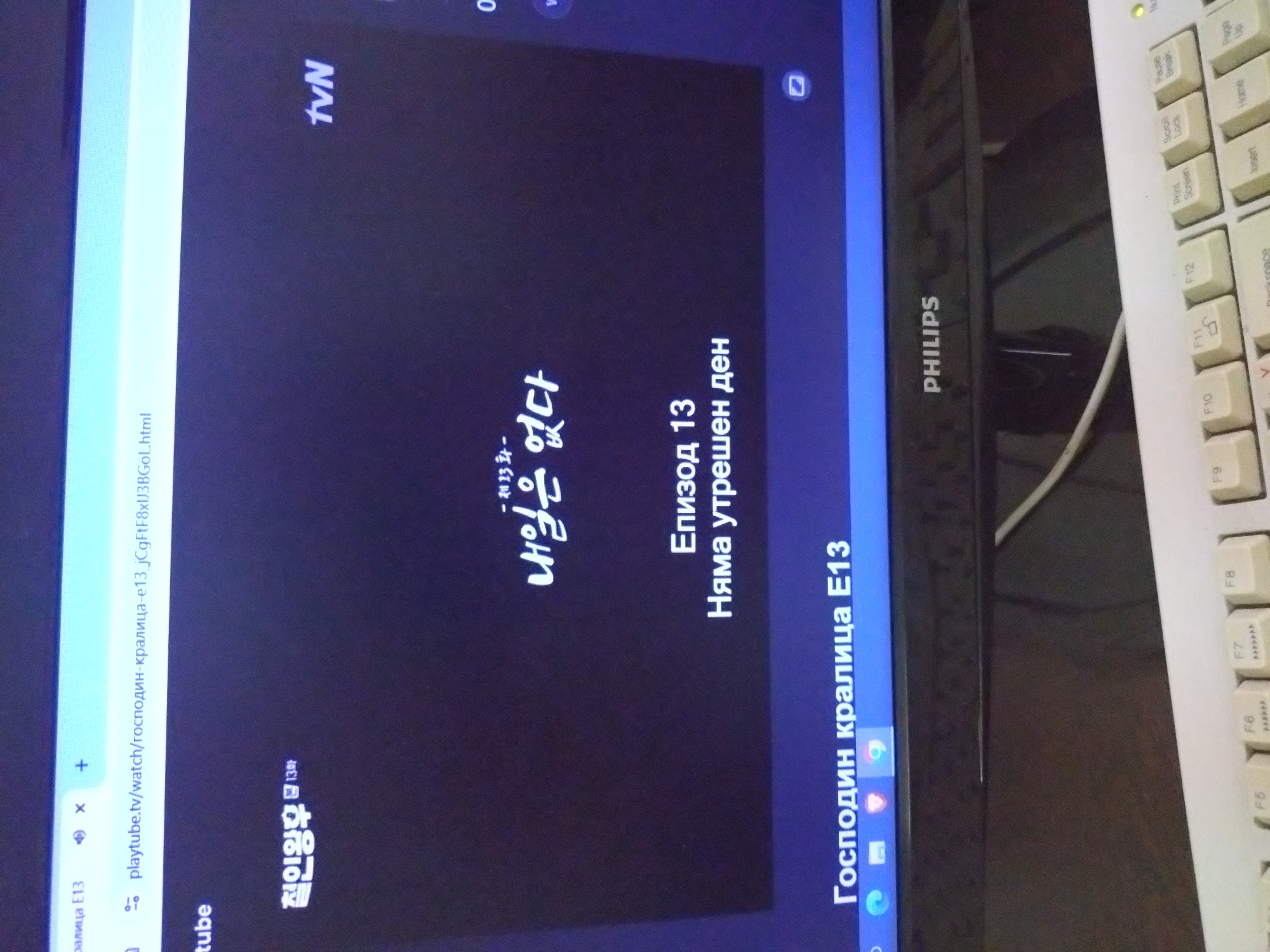 A Philips laptop displays a video streaming from "playtube.tv". The browser tab is titled "господин-кралица-e13", which translates to "Mr. Queen-e13". The video is an episode of the TVN series "Mr. Queen," specifically episode 13, with the Korean title "철인왕후 13화." The video also includes the text "-제13화-내일은 없다," translating to "-Episode 13-There is no tomorrow." The Cyrillic text on screen reads "Епизод 13 Няма утрешен ден Господин кралица Е13," indicating the episode is being watched in a language where that text is relevant, possibly Russian or Bulgarian. The laptop sits beside a beige keyboard. The location is not apparent from the image.