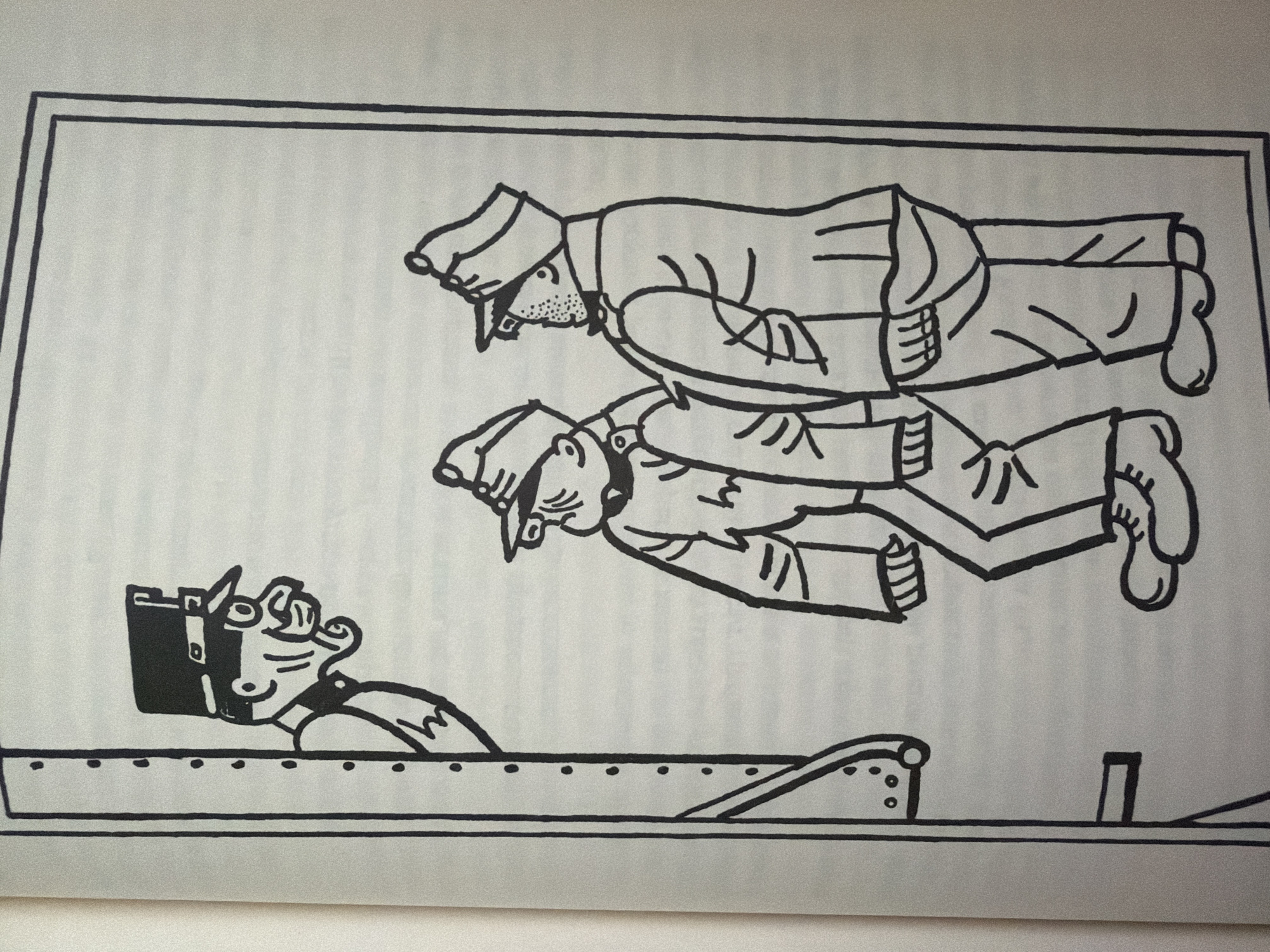 The image is a black and white line drawing depicting a scene with three cartoonish figures. On the left, a figure wearing a tall, dark hat with a brim and a uniform is peering out from behind a vertical structure. This figure has exaggerated facial features, including a prominent nose and mouth, and appears to be speaking or shouting. To the right, two other figures, also wearing similar hats and uniforms, stand facing away from the viewer. They are positioned next to each other. The figure on the left of this pair has his arms crossed. The background is a plain, light color, suggesting an indoor or nondescript outdoor setting. The drawing style is simplified with bold outlines. The image is presented as a page from a book, with faint lines and texture visible in the background. There is no identifiable location in the city of Pazardzhik, Bulgaria, depicted in this image.