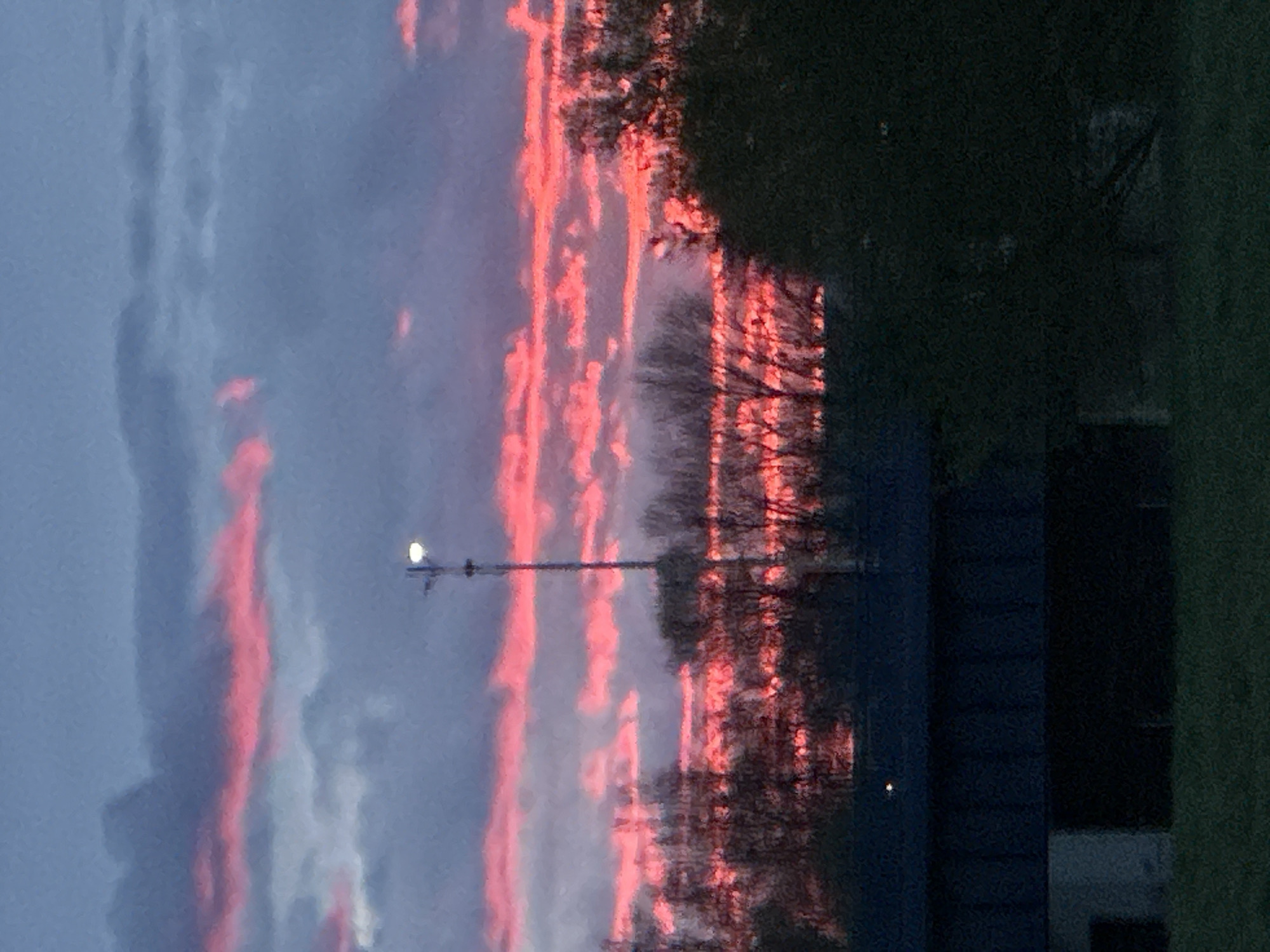 The image shows a sunset with pink clouds in the sky. In the foreground, there's a building, some trees, and a light pole. The specific location within the City of Zagreb, Croatia, is not discernible from the image.