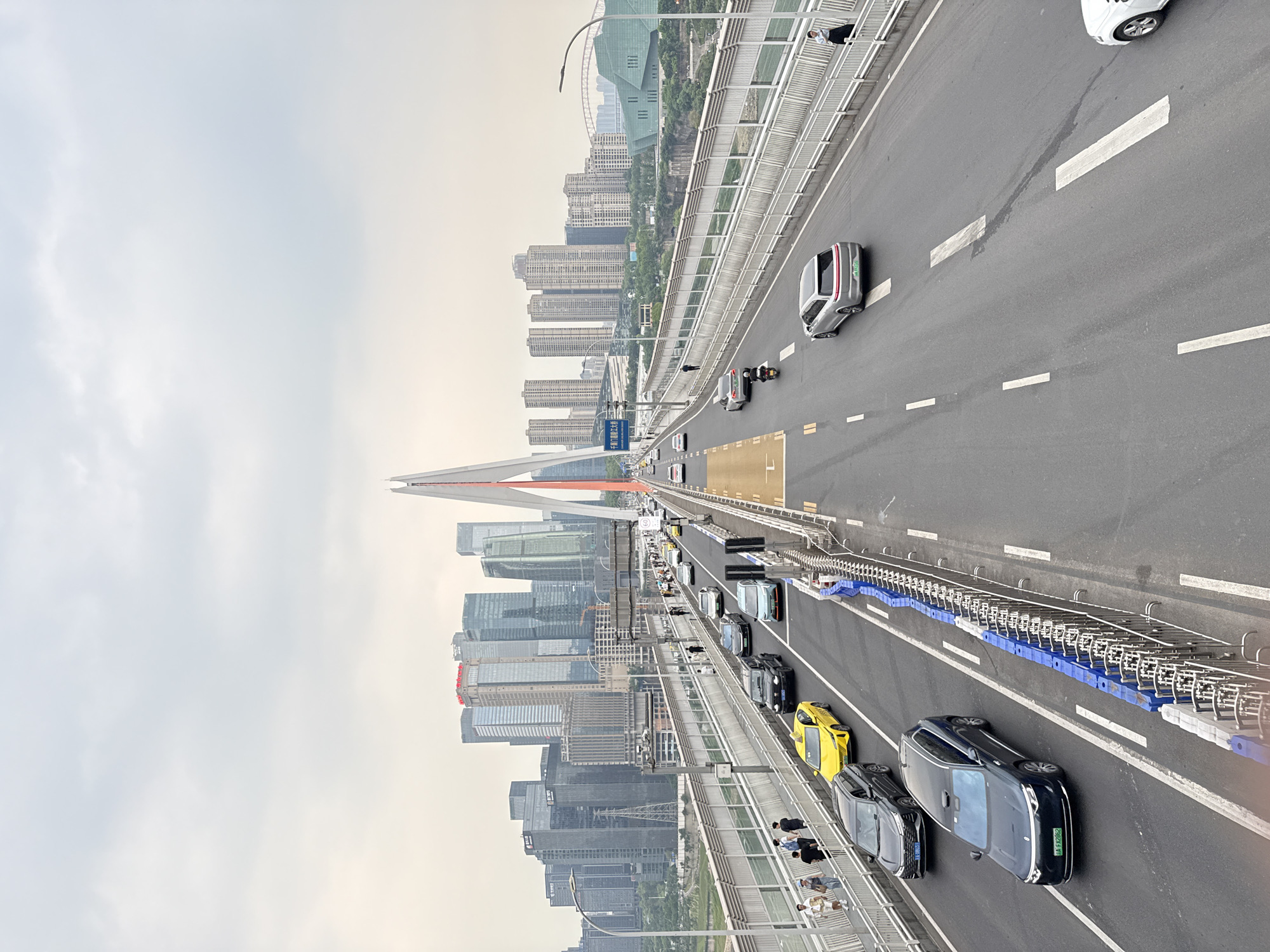 The image depicts a bridge in Yuzhong District, Chongqing, China. On the bridge, there is automobile and pedestrian traffic. The architecture of Yuzhong District is visible in the background. The sky is overcast.