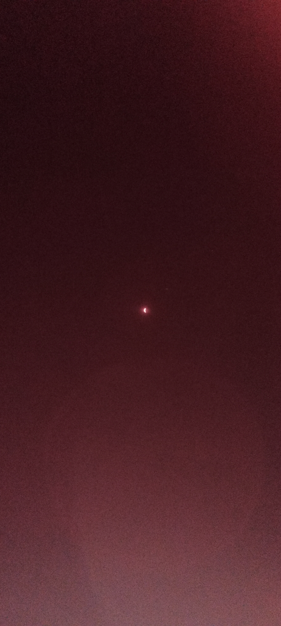 This media file is a photograph of a partial solar eclipse. The main subject is the crescent-shaped sun, visible as a small, bright object in the center of the frame. The surrounding scene is a dark, reddish-brown sky, likely due to atmospheric conditions or camera settings. There are no people or identifiable objects present.
The activity taking place is an astronomical event – a solar eclipse. The image captures a moment when the moon is partially obscuring the sun. The time of day is likely during daylight hours, but the darkness of the sky suggests it might be twilight or the eclipse has significantly dimmed the sunlight. There are no specific weather cues visible, beyond the general atmospheric haze indicated by the sky's color. Location cues for Adai, Spain are not apparent in the image itself.
Notable details include the sharp, bright crescent of the sun against the muted background. A faint, smaller point of light is also visible slightly above and to the right of the main eclipse. The overall impression is one of cosmic wonder and observation of a celestial phenomenon. No visible text is present in the image.