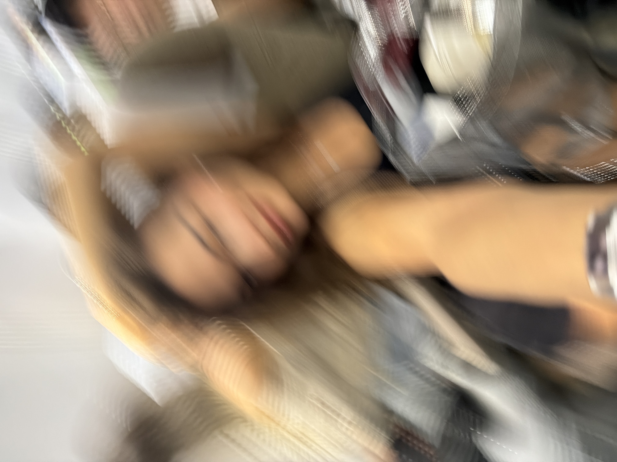 The image appears to be a blurred and rotated photograph of a person lying down. Facial features are partially visible, including the nose and lips. The person has blonde hair. They are wearing a light-colored top. There is some clothing visible nearby, and an object that appears to be made of metal and mesh. The location, Ban Kho En, Thailand, is not discernible from the image. There are no clear actions, interactions, or environmental details that can be ascertained from the picture.