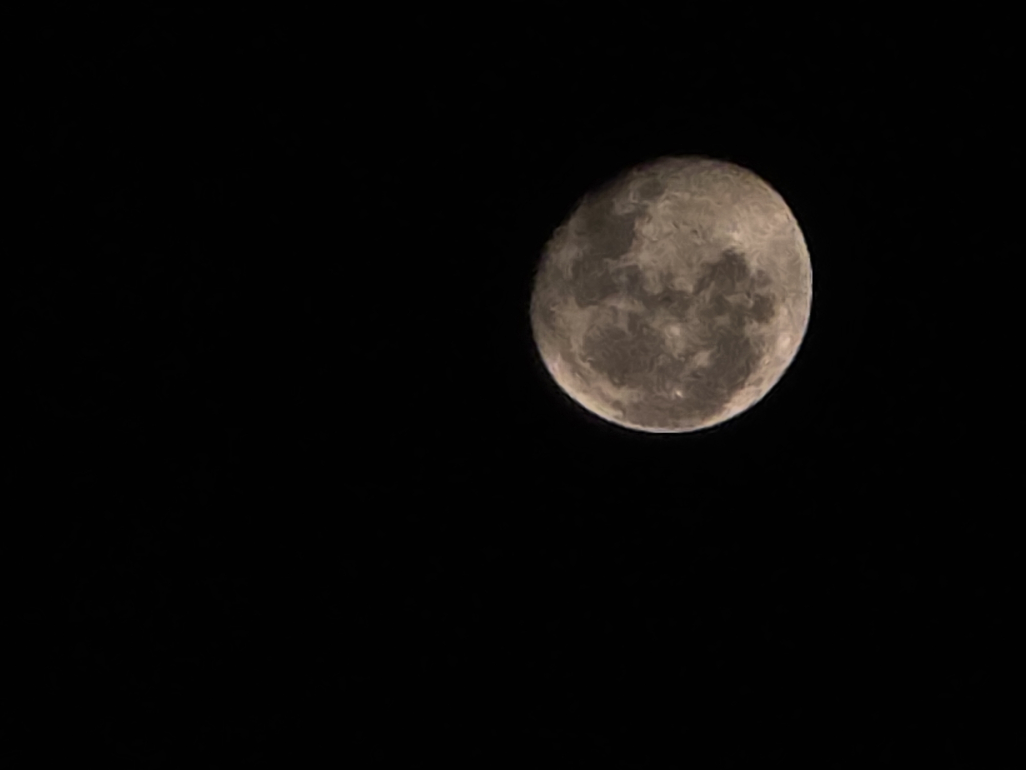 A full moon is visible in a dark sky, occupying the lower right portion of the frame. The moon's surface shows craters and maria, with variations in light and shadow creating a textured appearance. The background is entirely black, suggesting a nighttime scene with no other celestial bodies or atmospheric elements visible. The image is a close-up of the moon against a void.