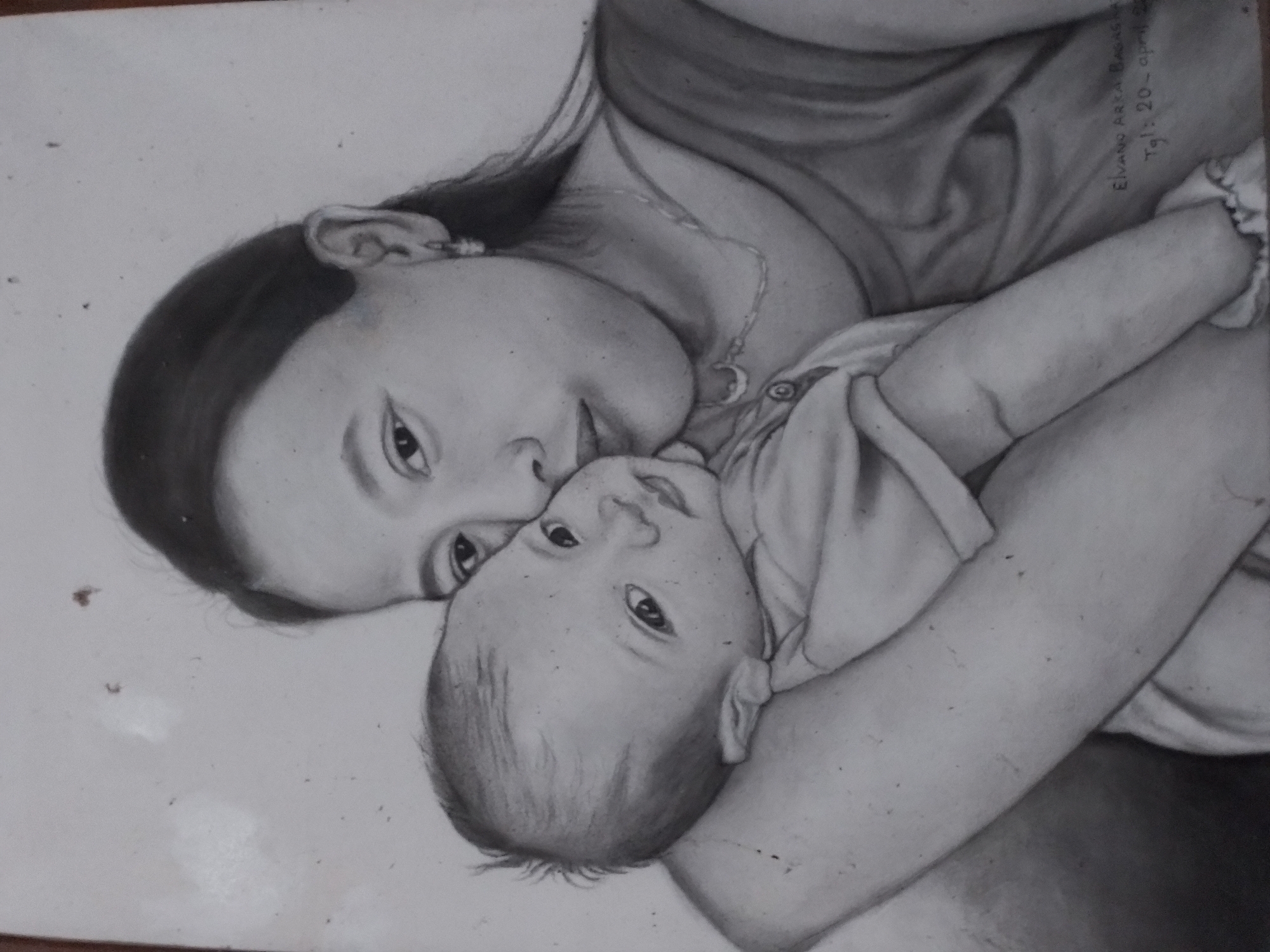 A black and white drawing depicts a woman holding a baby. The woman is on the right side of the frame, looking towards the left. She has dark hair pulled back and is wearing a sleeveless top and a necklace. She is embracing the baby who is held in her arms, with the baby's head resting on her shoulder. The baby is facing the viewer and appears to be looking slightly to the left. The baby is wearing a light-colored garment. There is writing in the bottom right corner of the drawing which appears to be a signature and date. The background is plain and light-colored.