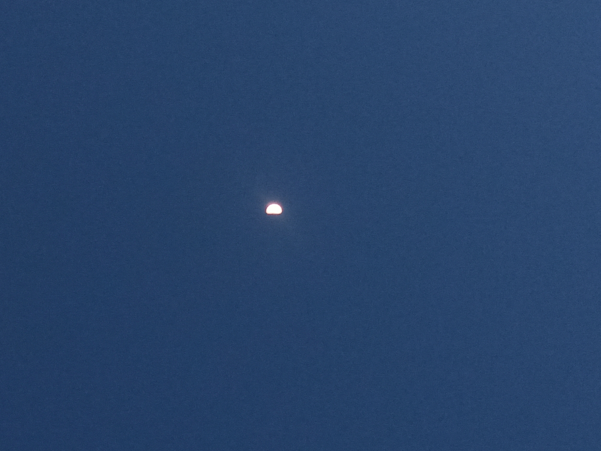The image shows a clear, dark blue sky with a crescent moon illuminated on the left side, centered slightly to the left of the frame. The moon appears to be in a waxing or waning gibbous phase, with approximately half of it visible. There are no other celestial bodies or objects discernible in the sky. The image is devoid of any ground features or urban elements, suggesting it was captured from an open area or at a high vantage point. The location specified in Tuba, Indonesia, is not discernible from the visual information within the image itself, as there are no contextual clues to indicate any specific geographical features or man-made structures. The photograph focuses solely on the moon against the vast expanse of the night sky.